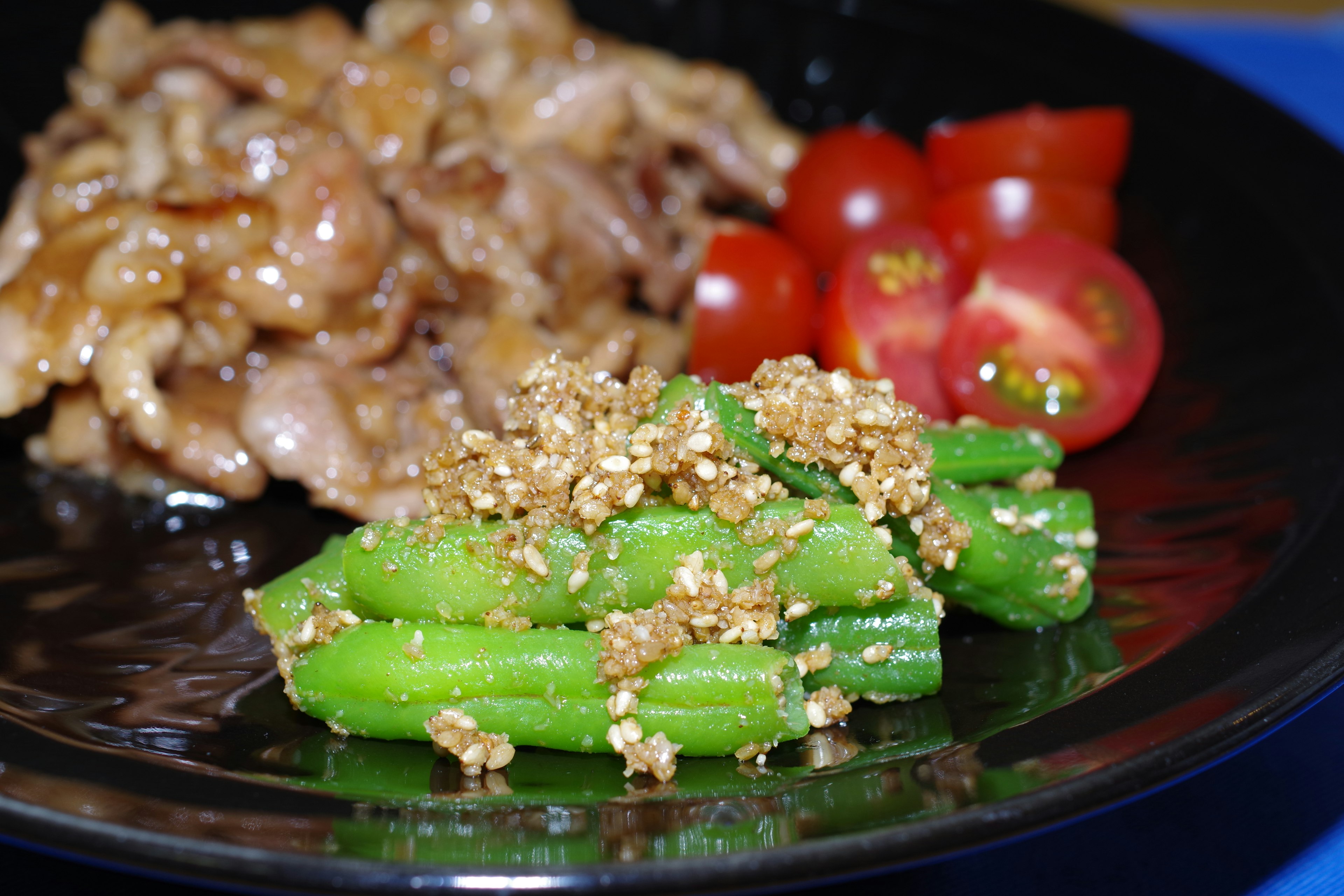 黑色盘子里的甜咸肉菜和芝麻青菜以及樱桃番茄