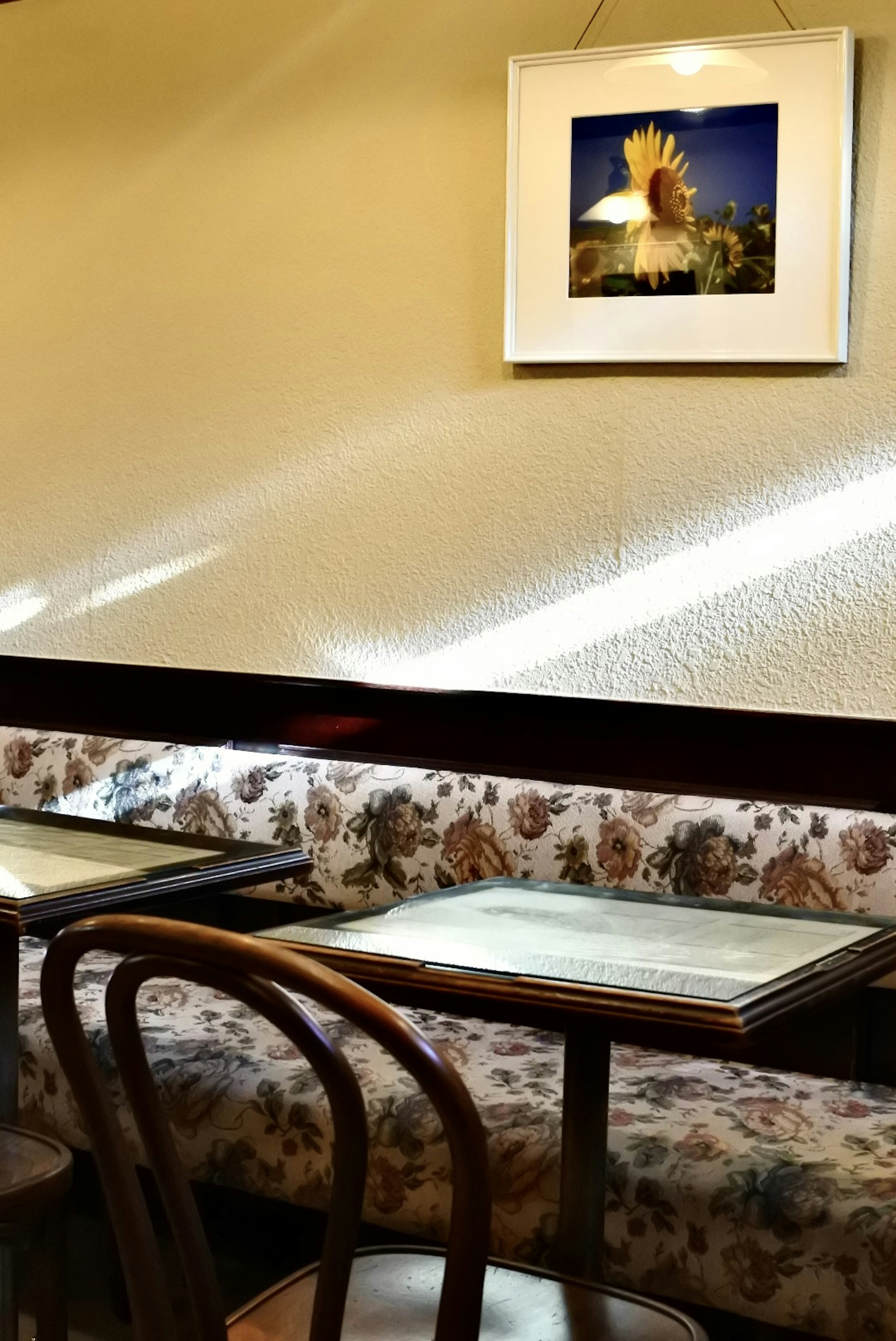 Interior de una cafetería con mesa y sillas y una foto de girasol en la pared