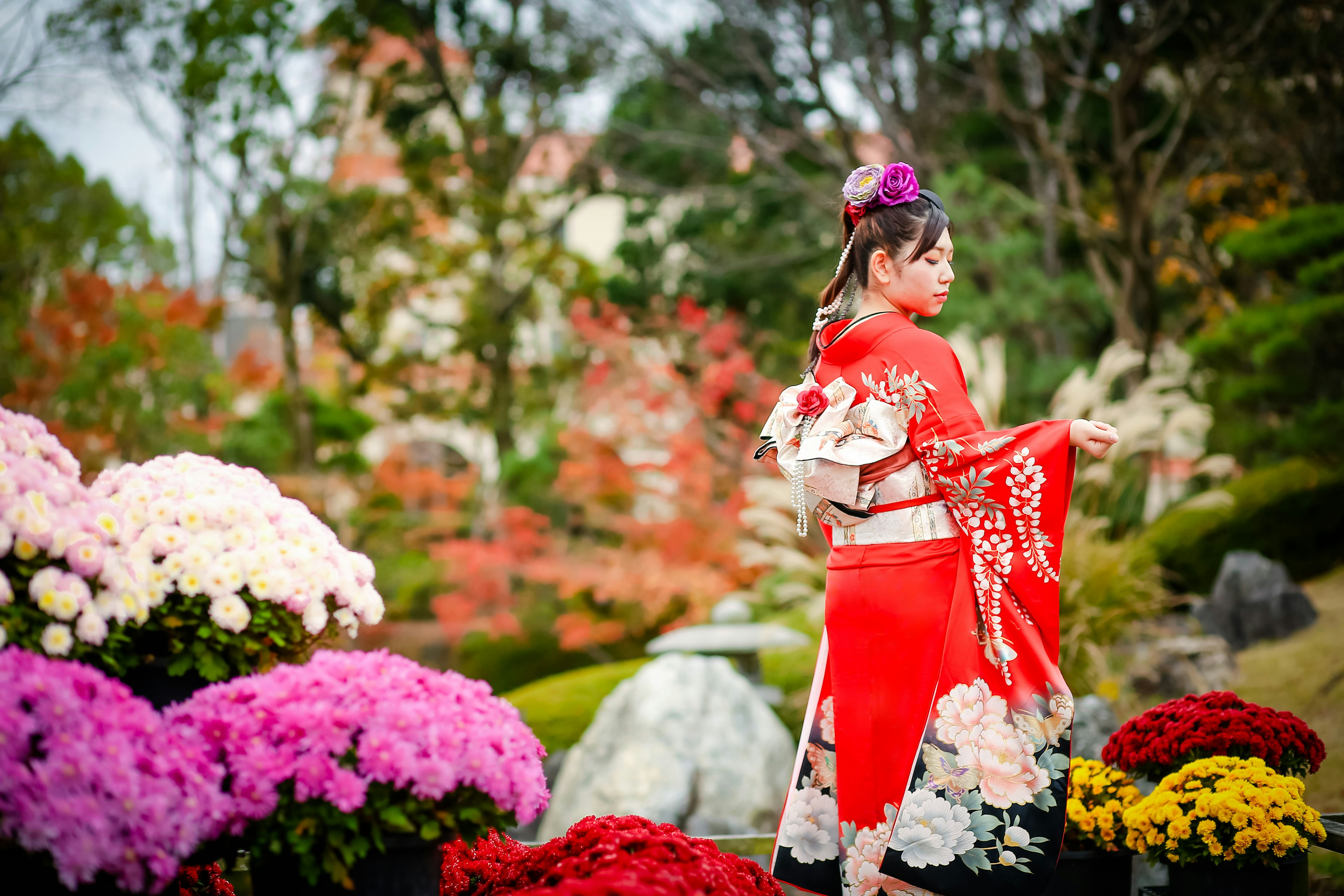 Eine Frau im roten Kimono steht zwischen bunten Blumen in einem schönen Garten