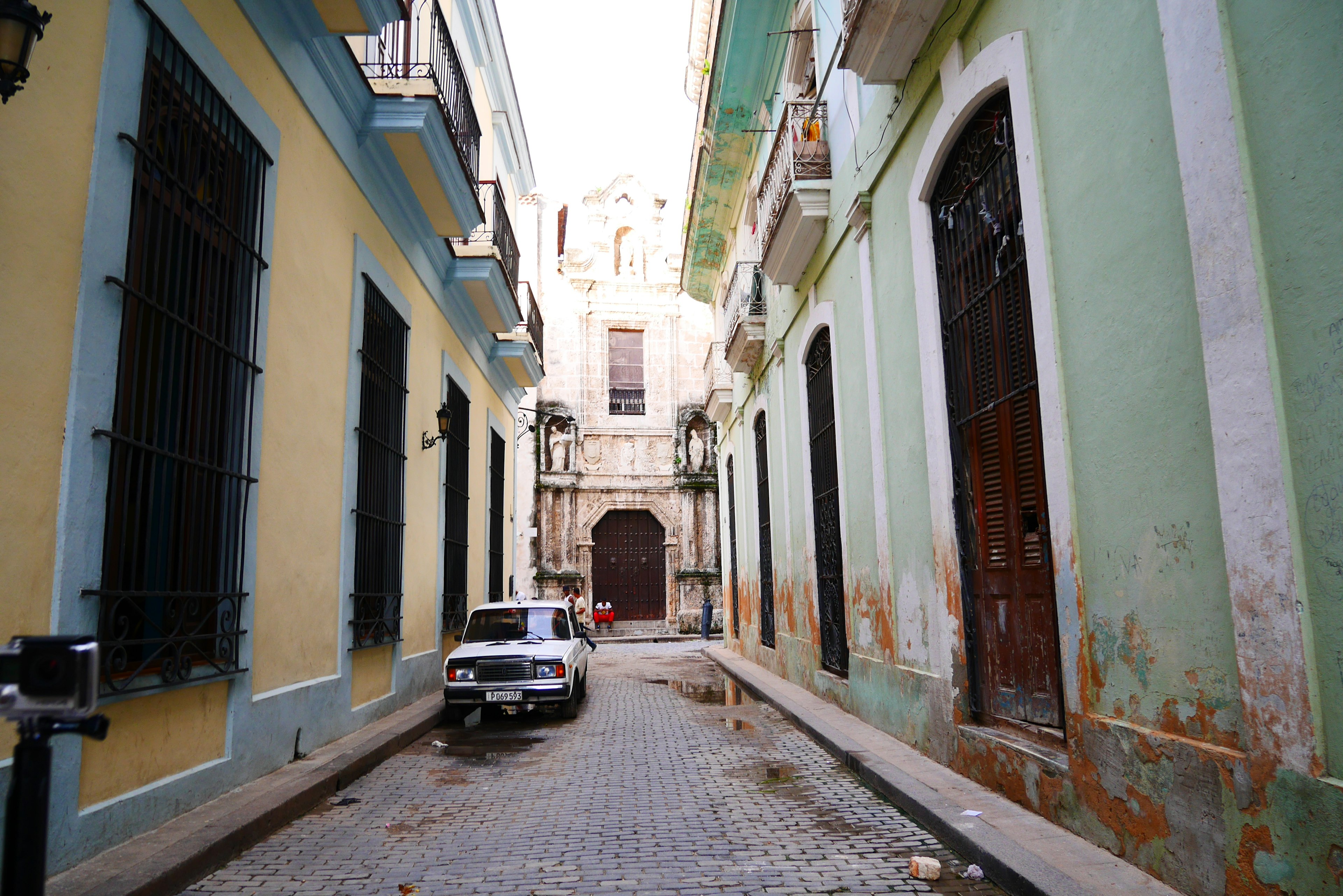 View of an old street with yellow and green buildings cobblestone path and a parked car