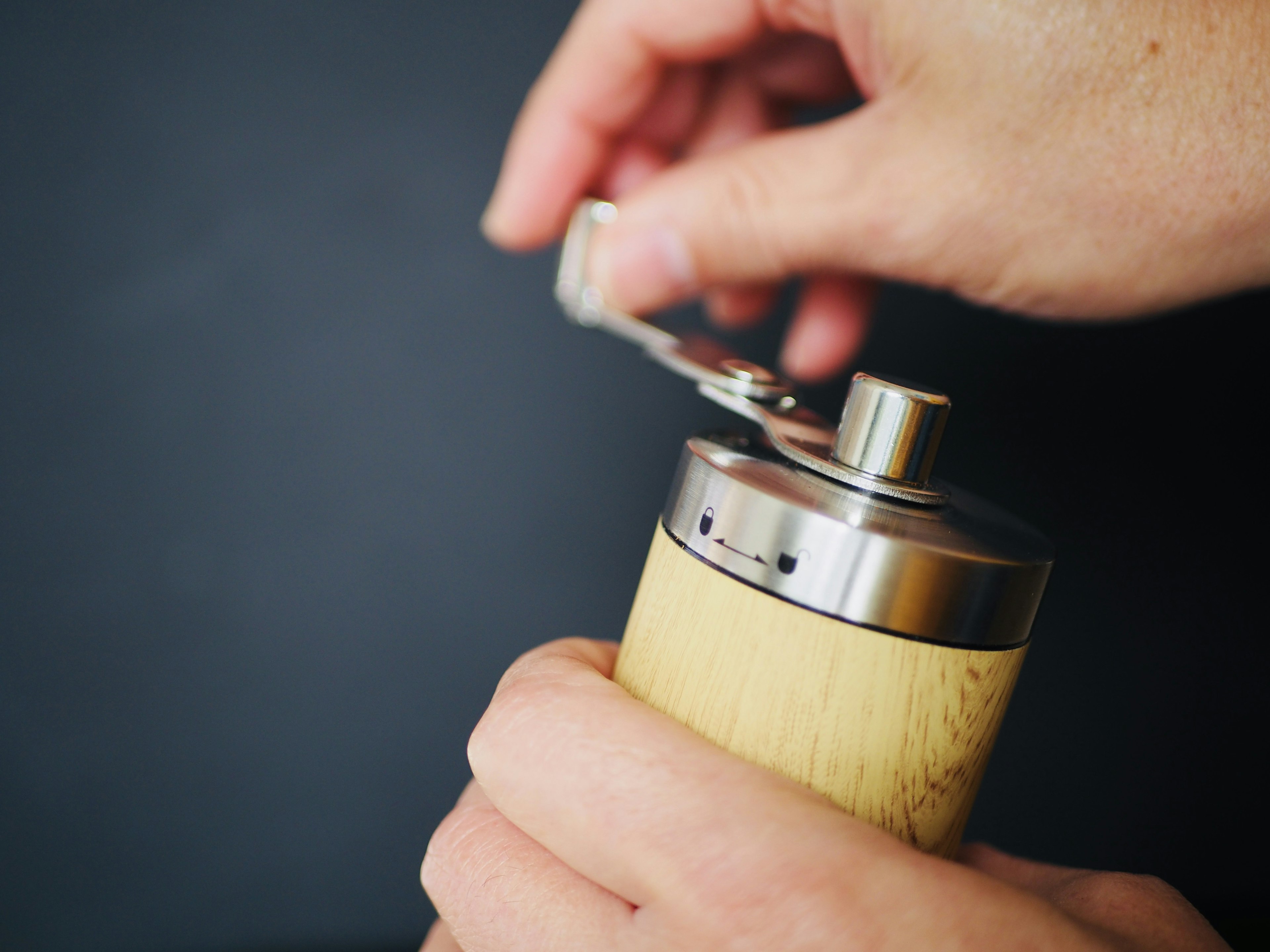 A hand adjusting the top of a wooden coffee grinder