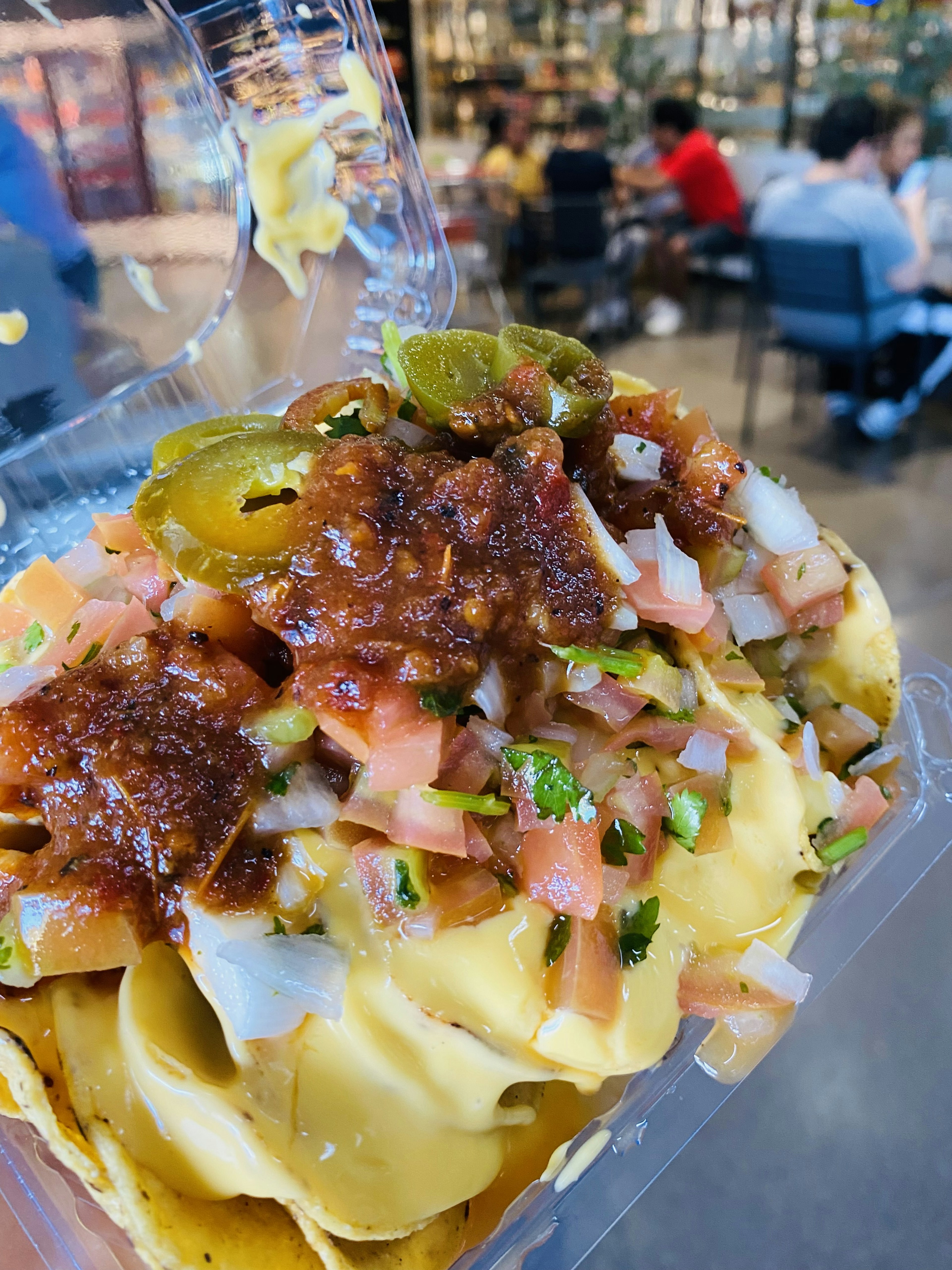 Nachos cubiertos con queso, tomates, cebollas y jalapeños en un recipiente transparente