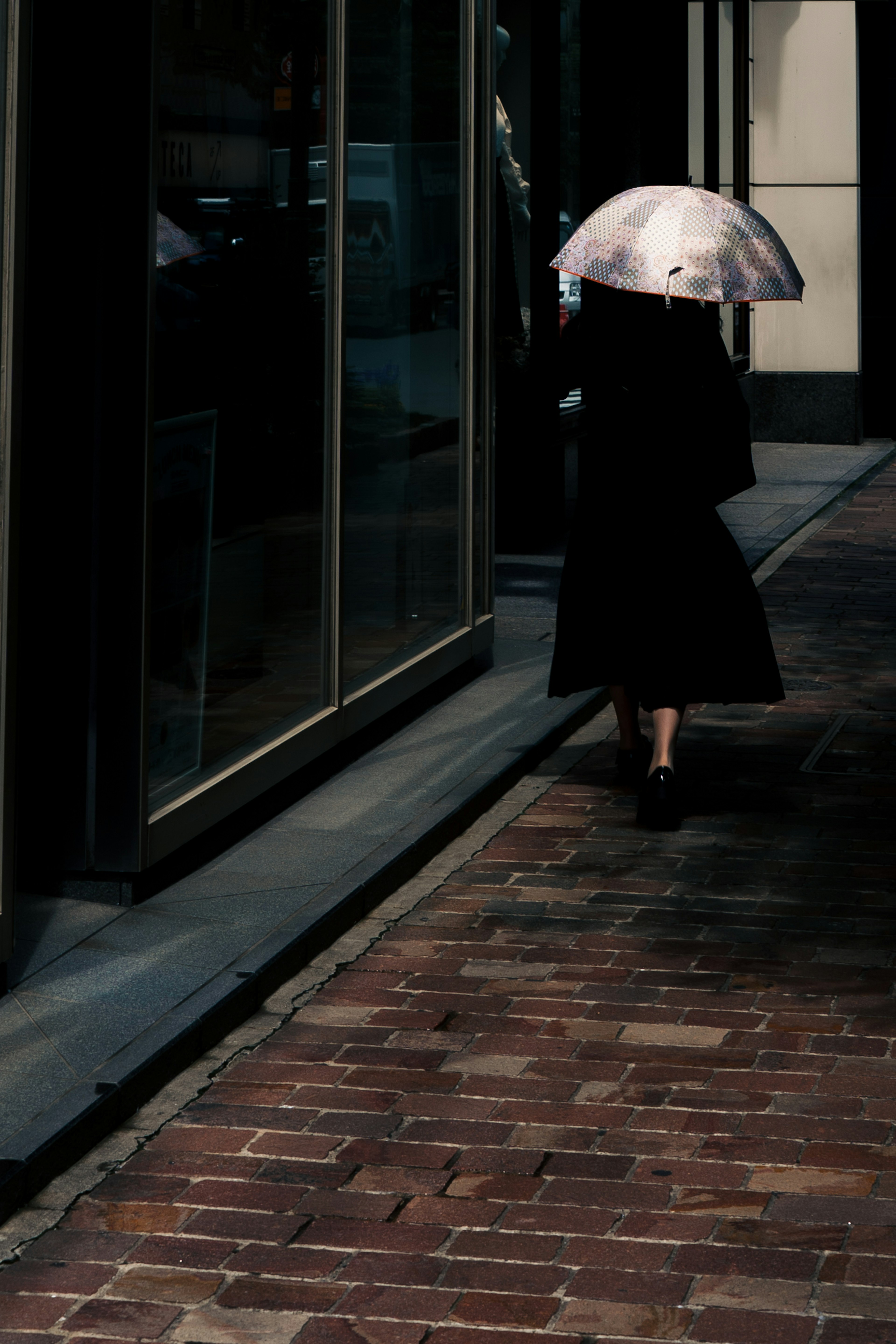 A person in black clothing walking with an umbrella on a cobblestone street