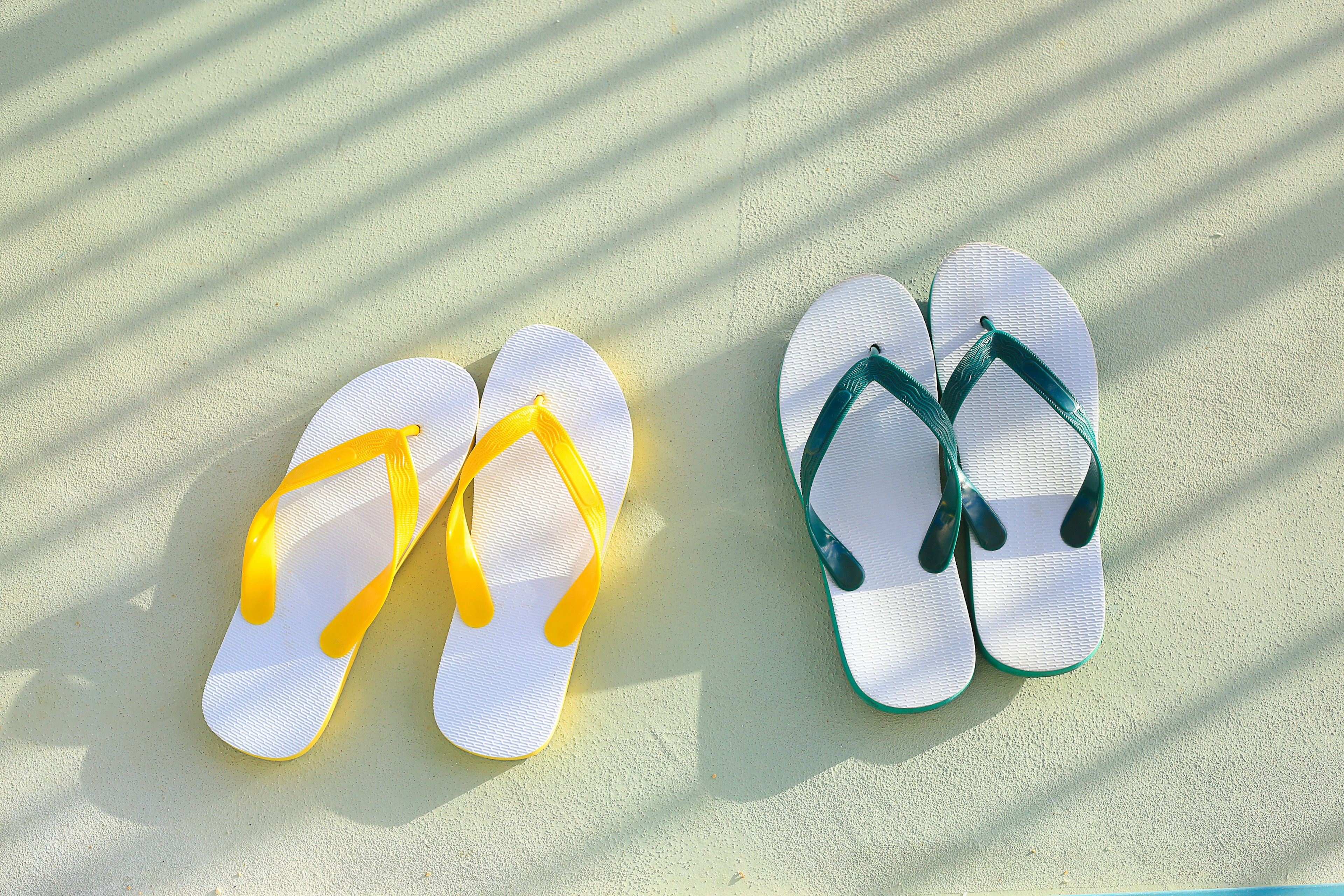 White flip-flops with yellow straps and green straps placed on a light surface