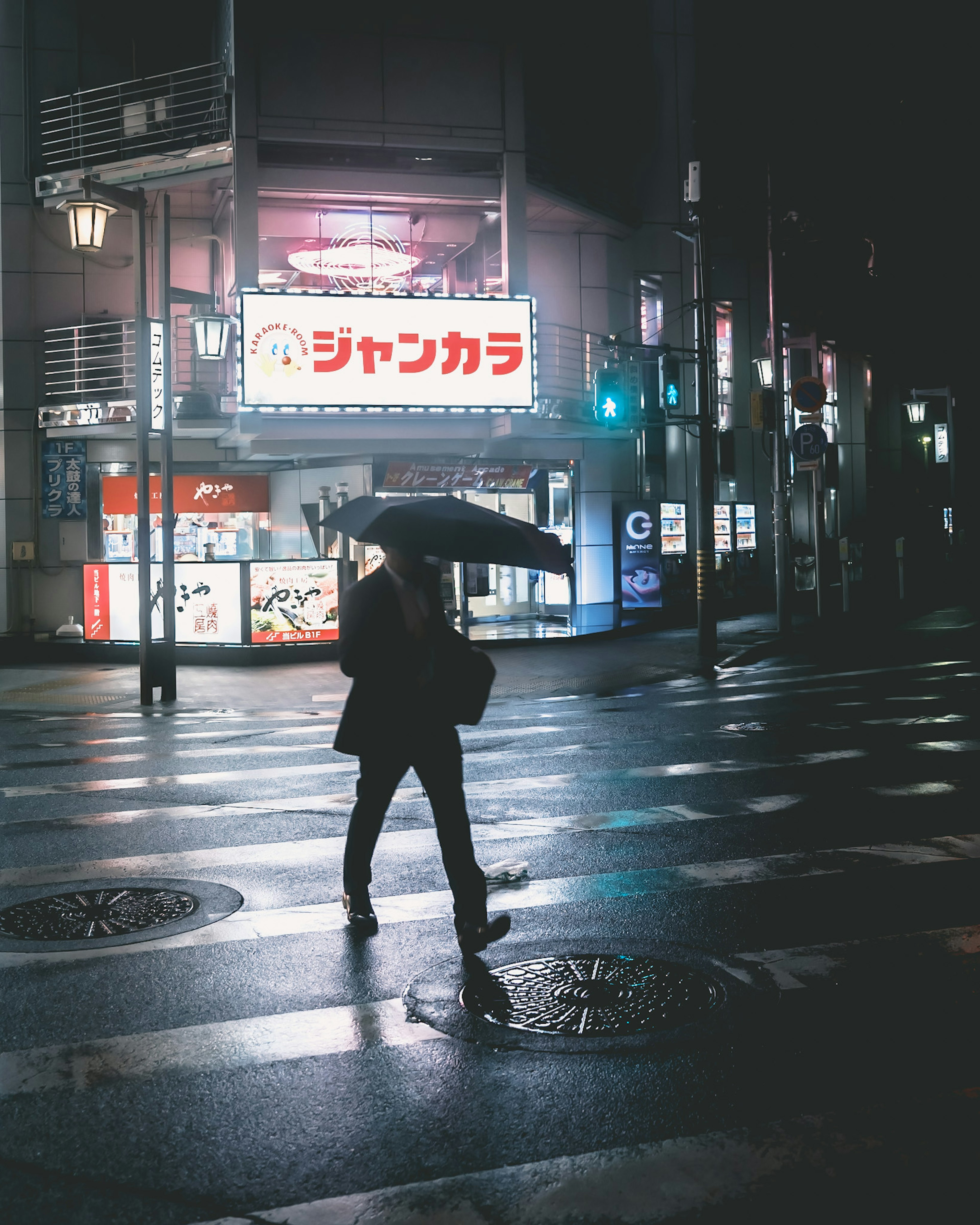 Eine Person, die mit einem Regenschirm in einer regnerischen Stadtstraße mit hellen Schildern geht