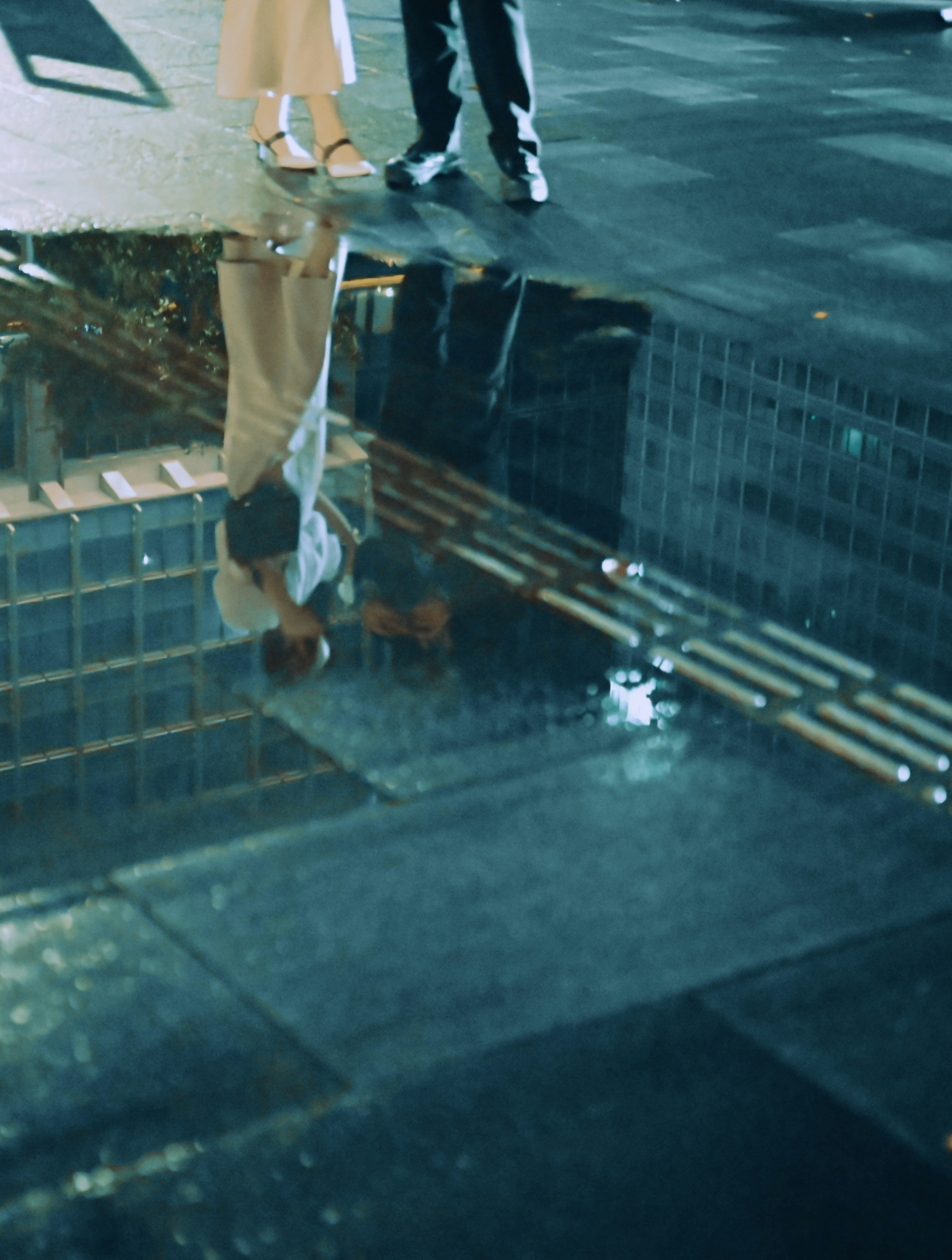 Reflections of people's feet and urban scenery in a puddle