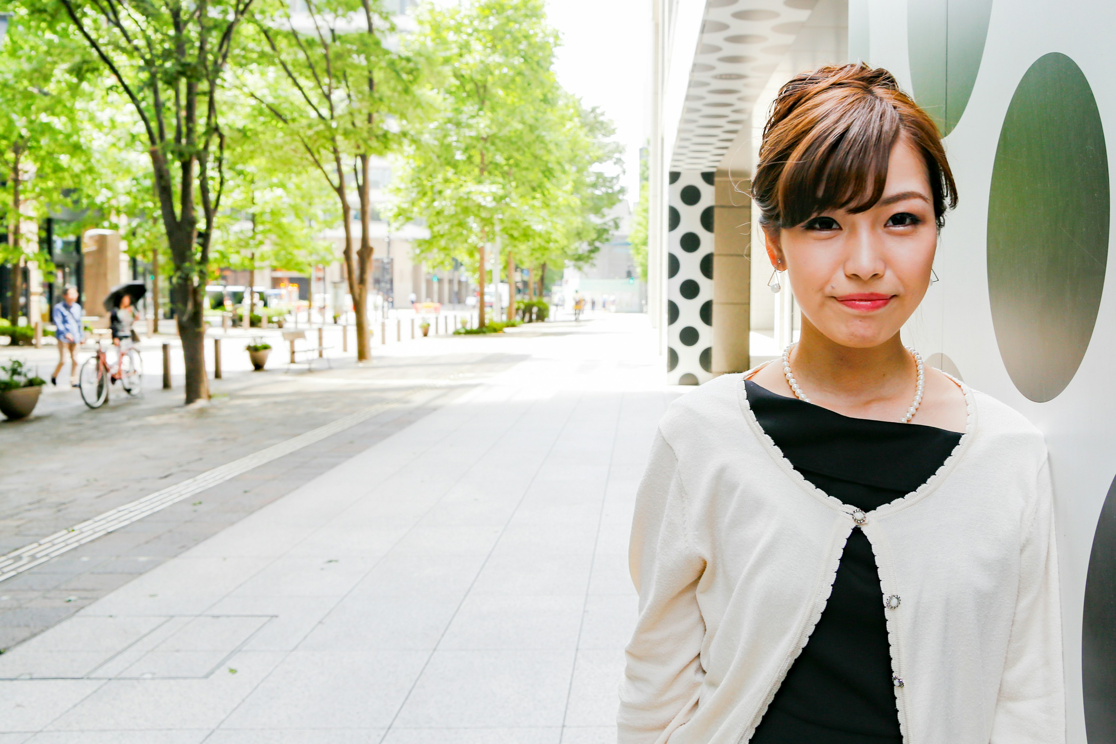 A woman smiling in the city with green trees in the background