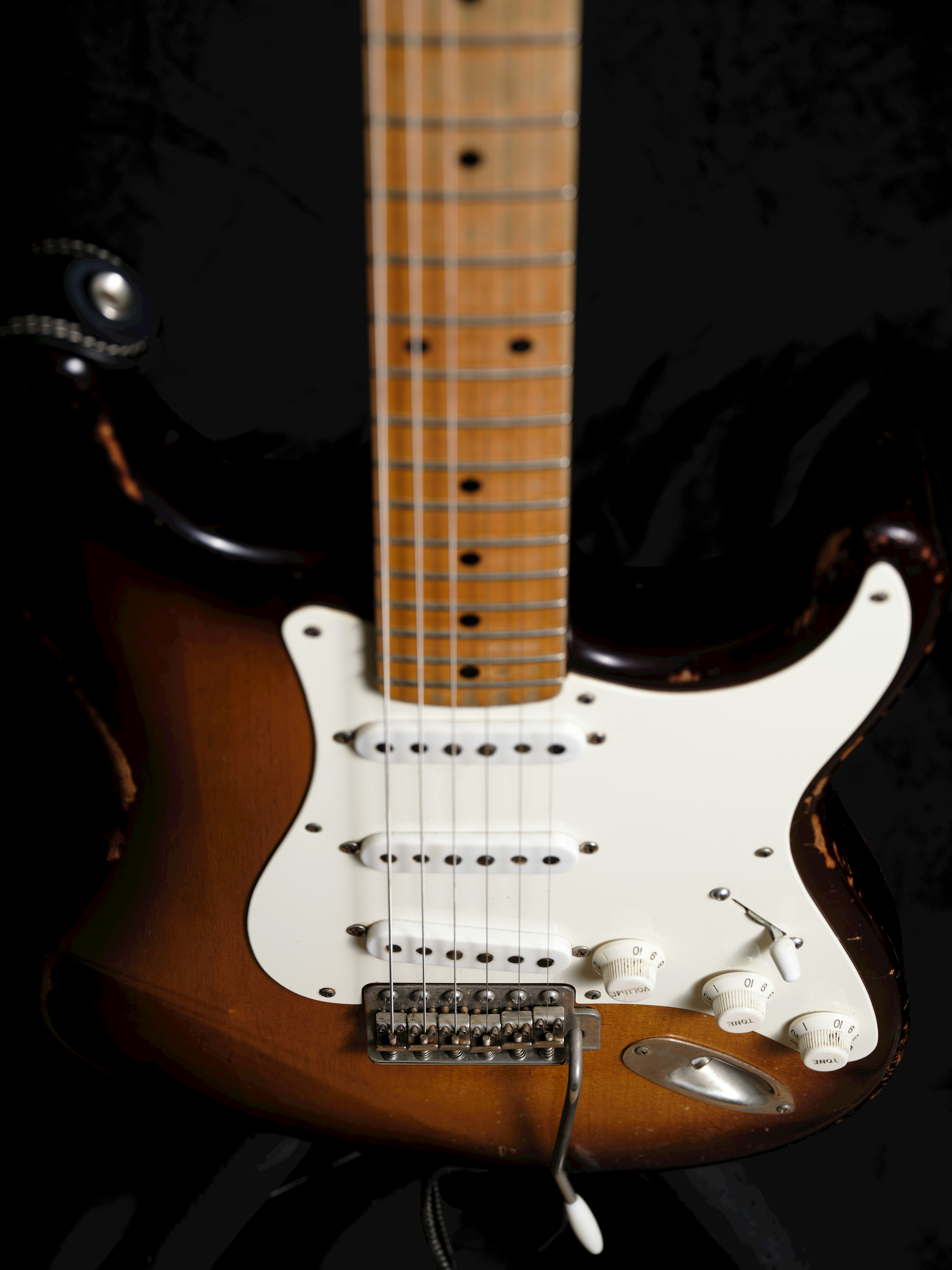 Close-up gitar listrik dengan nada coklat dan putih tipe Stratocaster