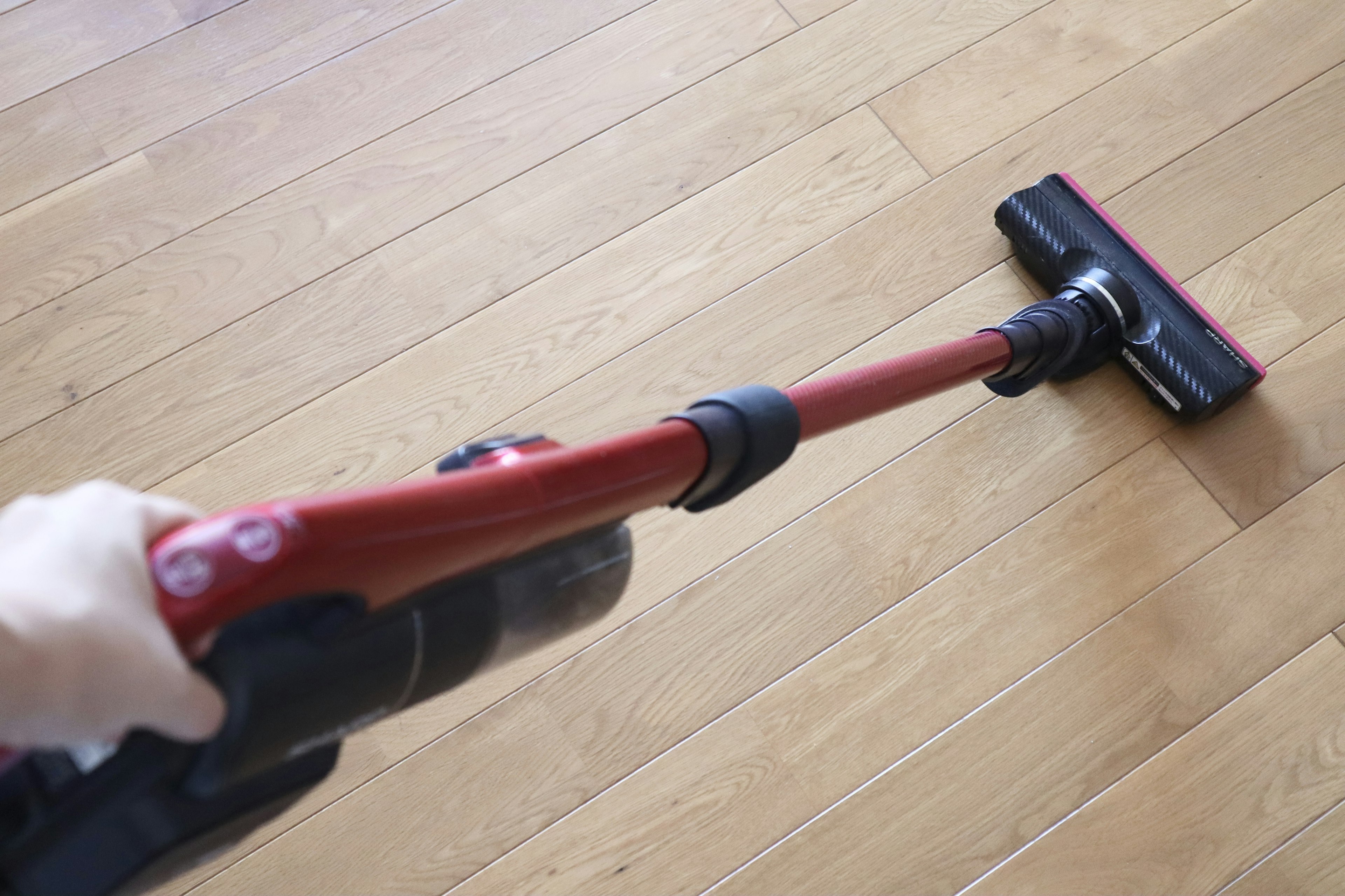 Una aspiradora de mano roja en uso sobre un suelo de madera