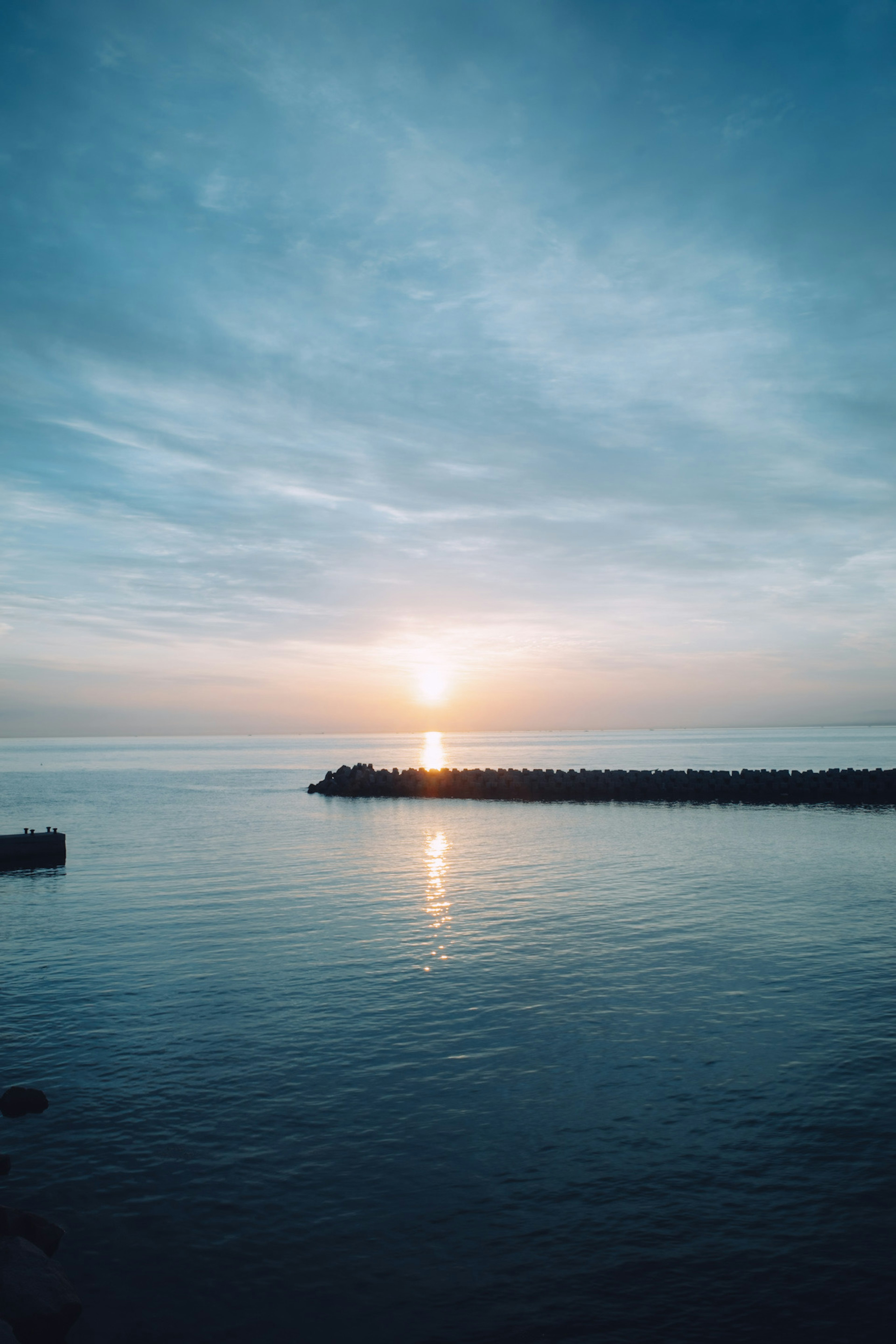 Sunset over calm waters with a rocky shoreline and soft clouds