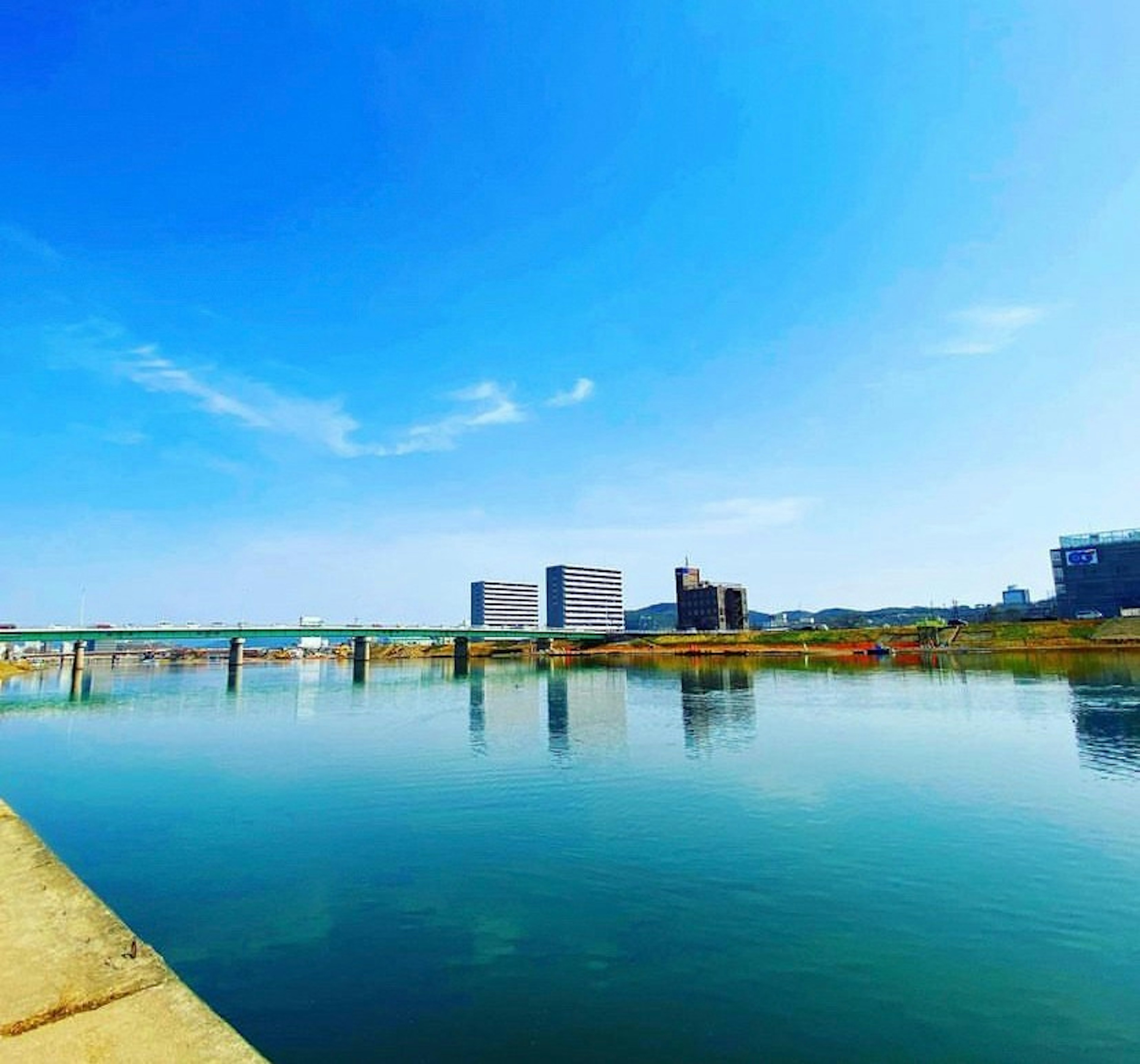 Río tranquilo reflejando el cielo azul con edificios en la orilla opuesta