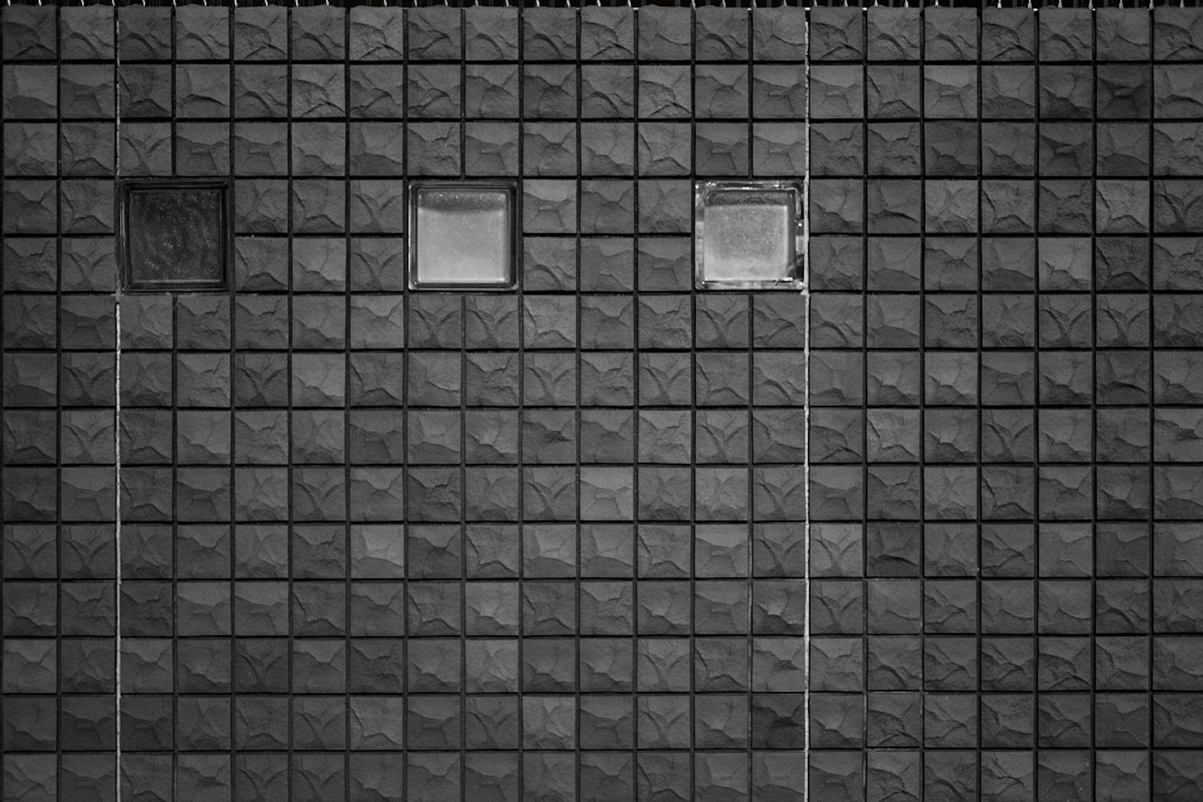 A wall covered with black and white tiles featuring three small windows