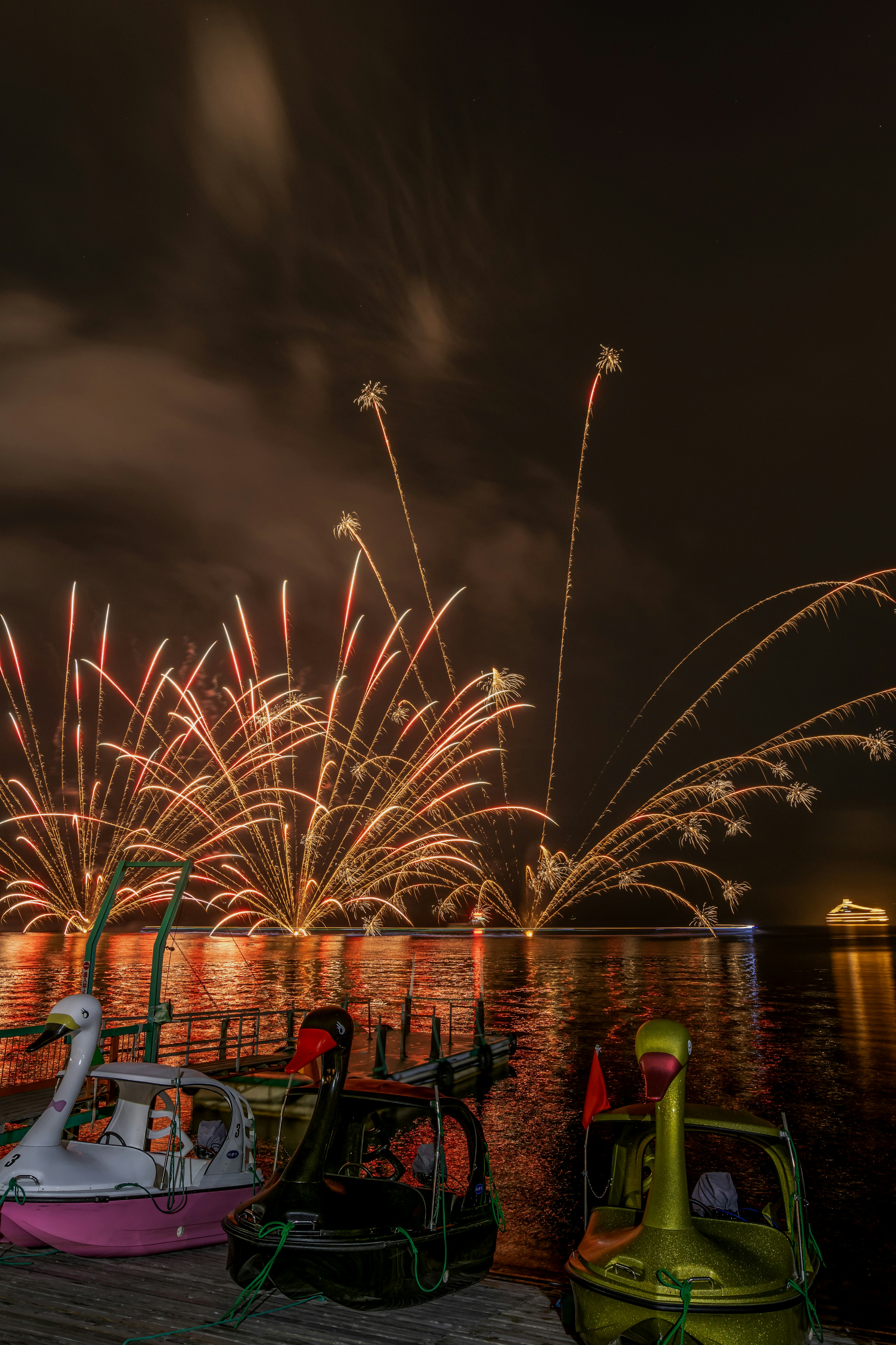 Colorful fireworks exploding in the night sky reflected on water with boats in the foreground