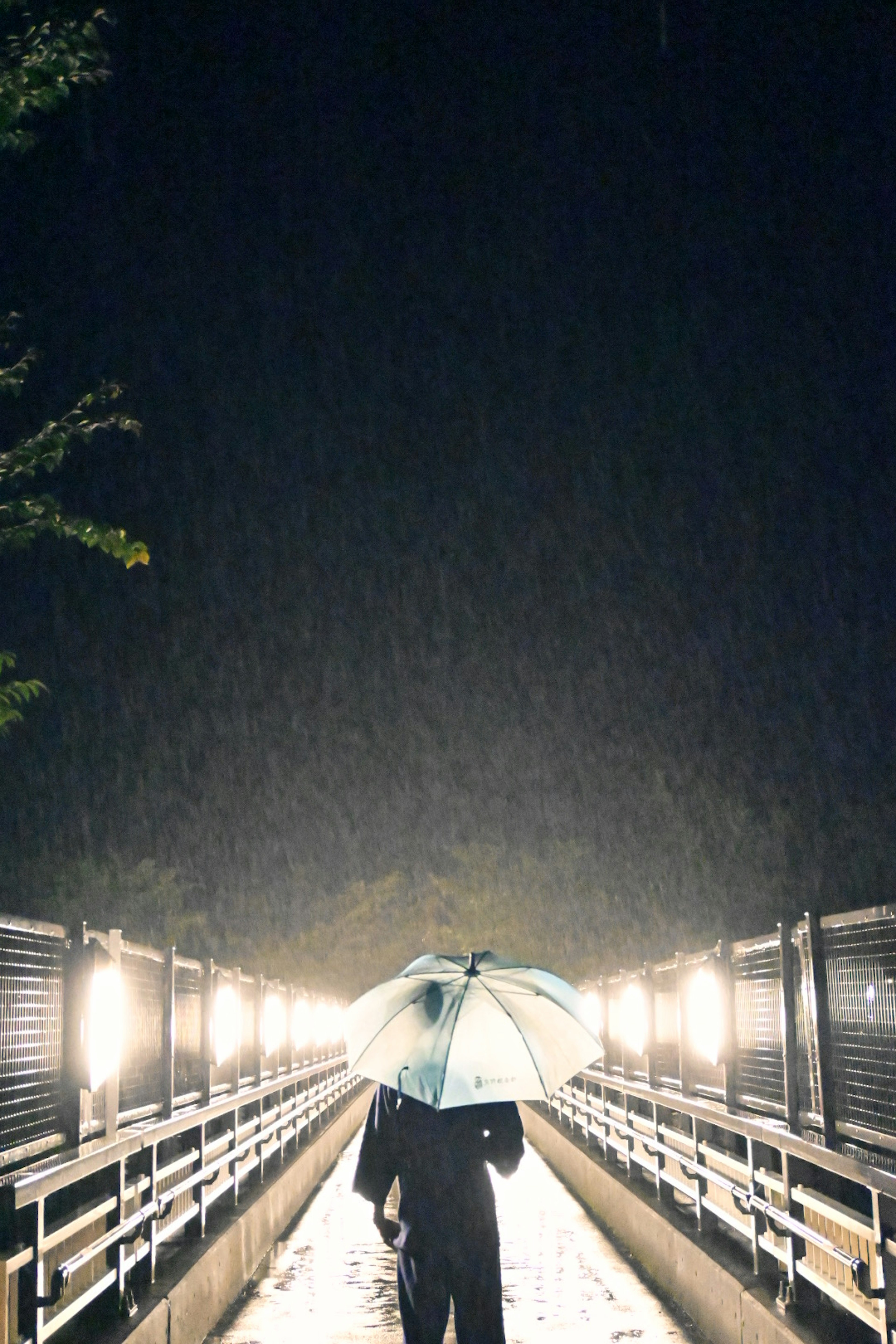 Una persona con un paraguas caminando sobre un puente iluminado por luces bajo la lluvia de noche