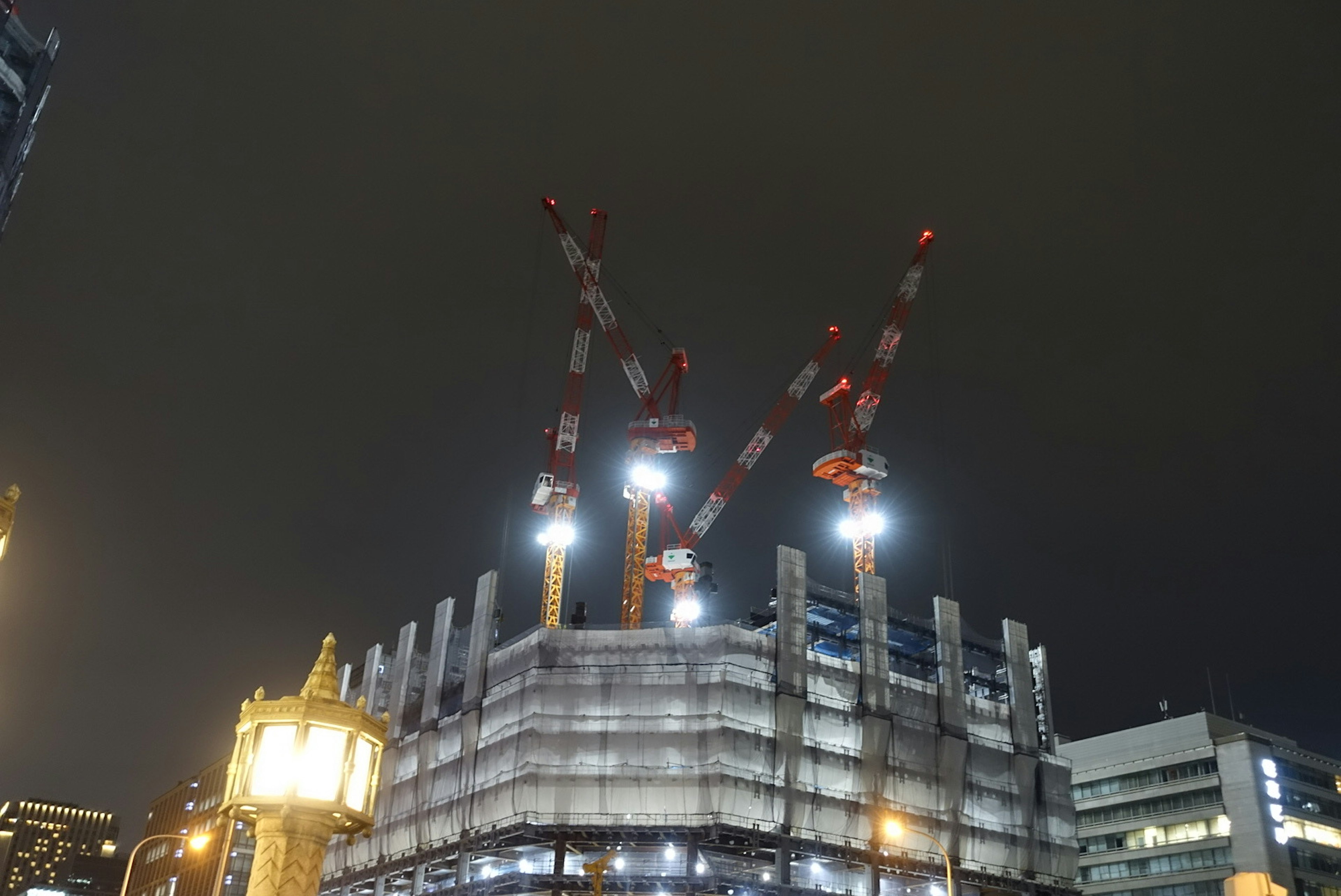 Site de construction la nuit avec des grues illuminées formant un W