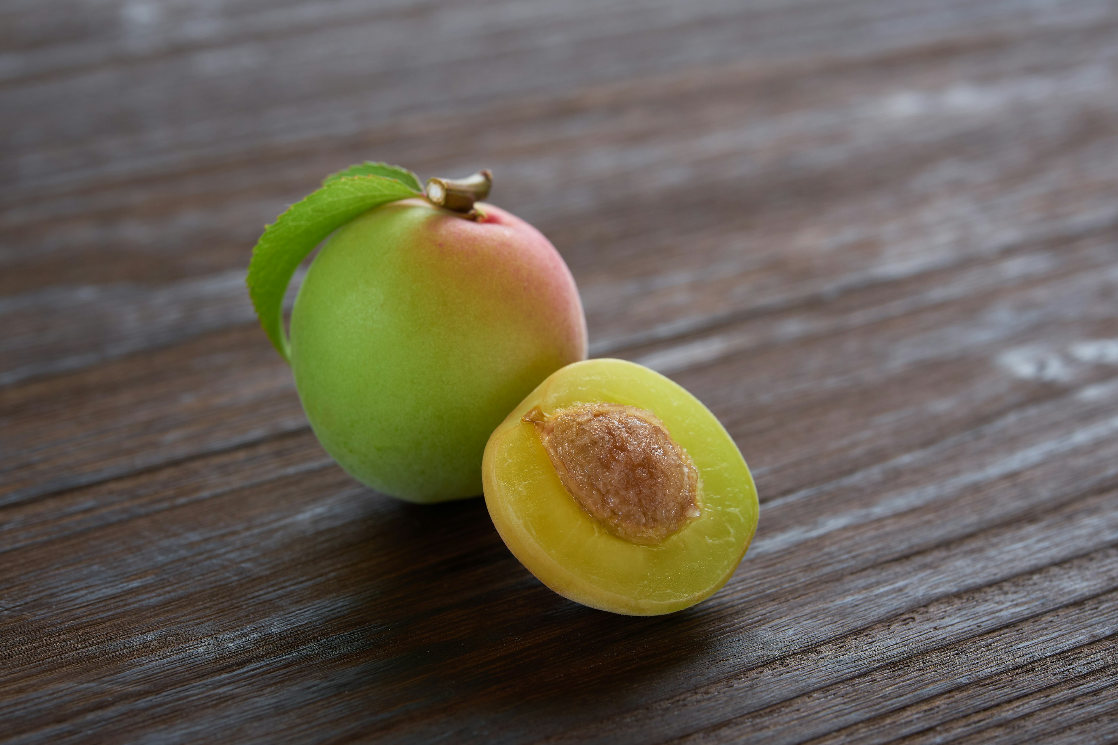 Green and pink plum with a cut section revealing the seed