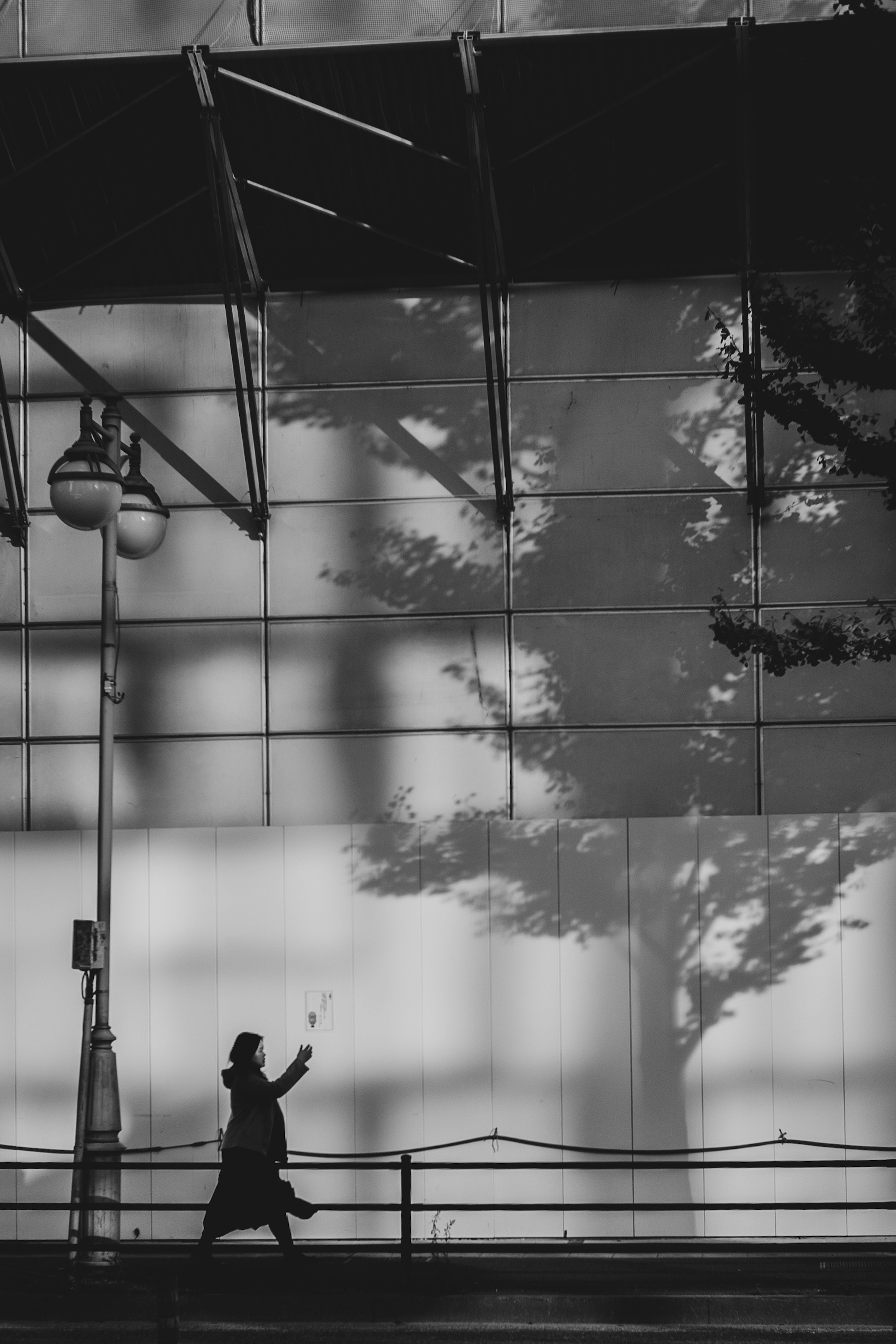 Une personne marchant en contraste noir et blanc avec des ombres projetées sur un mur en verre