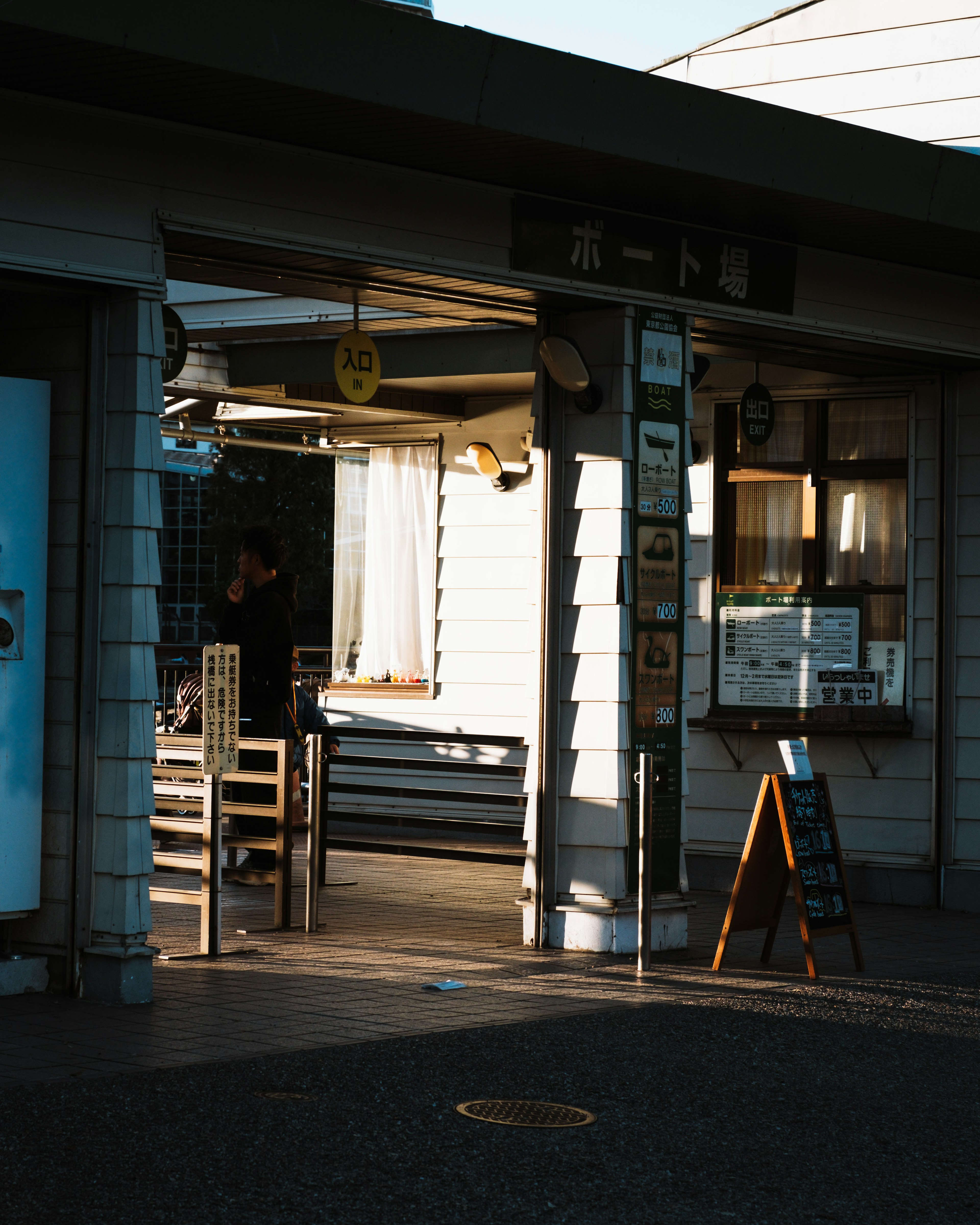 Entrada de una pequeña tienda iluminada por la luz del sol con sillas de madera y un letrero