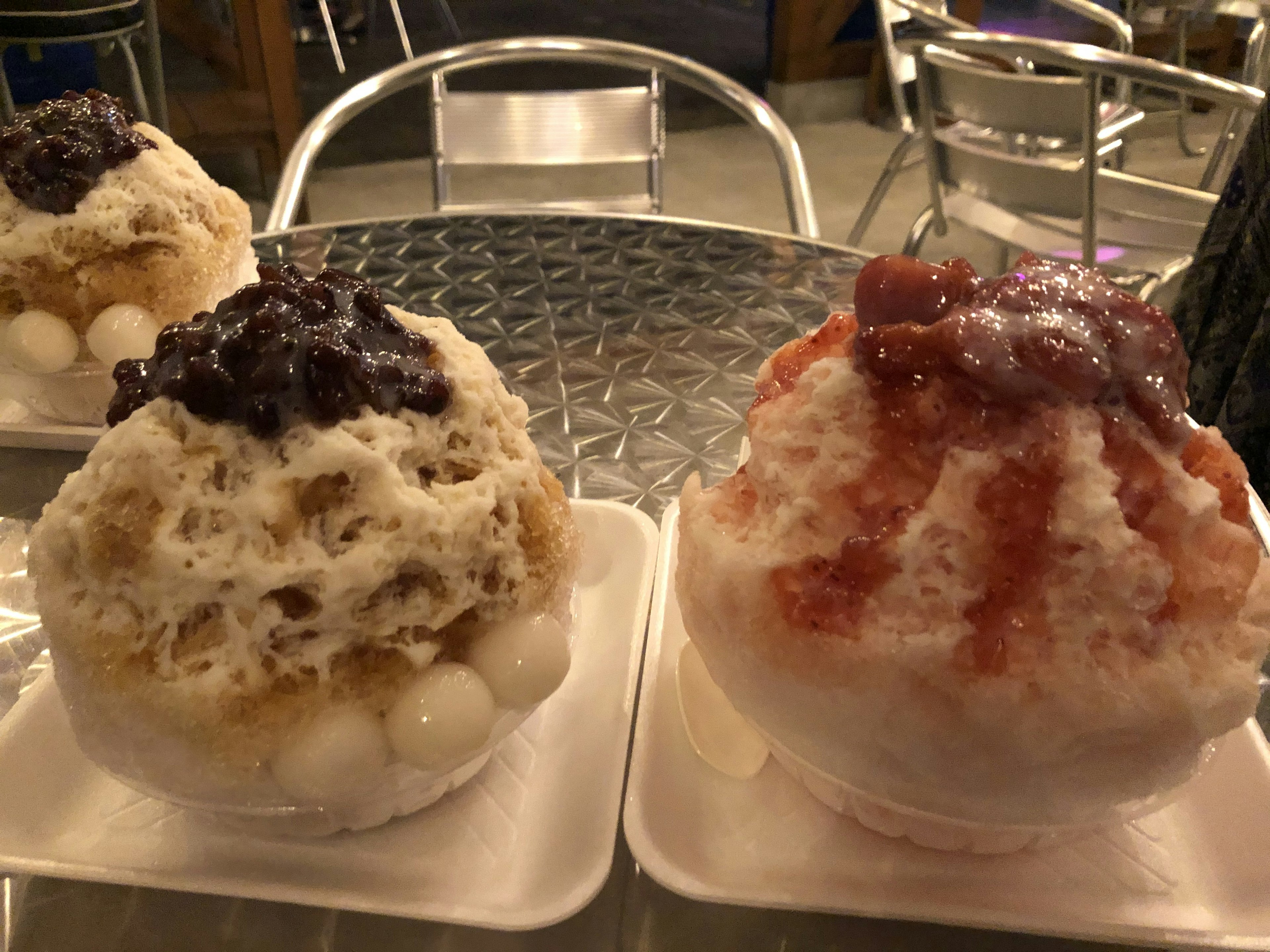 Two bowls of fluffy shaved ice topped with red bean and strawberry syrup