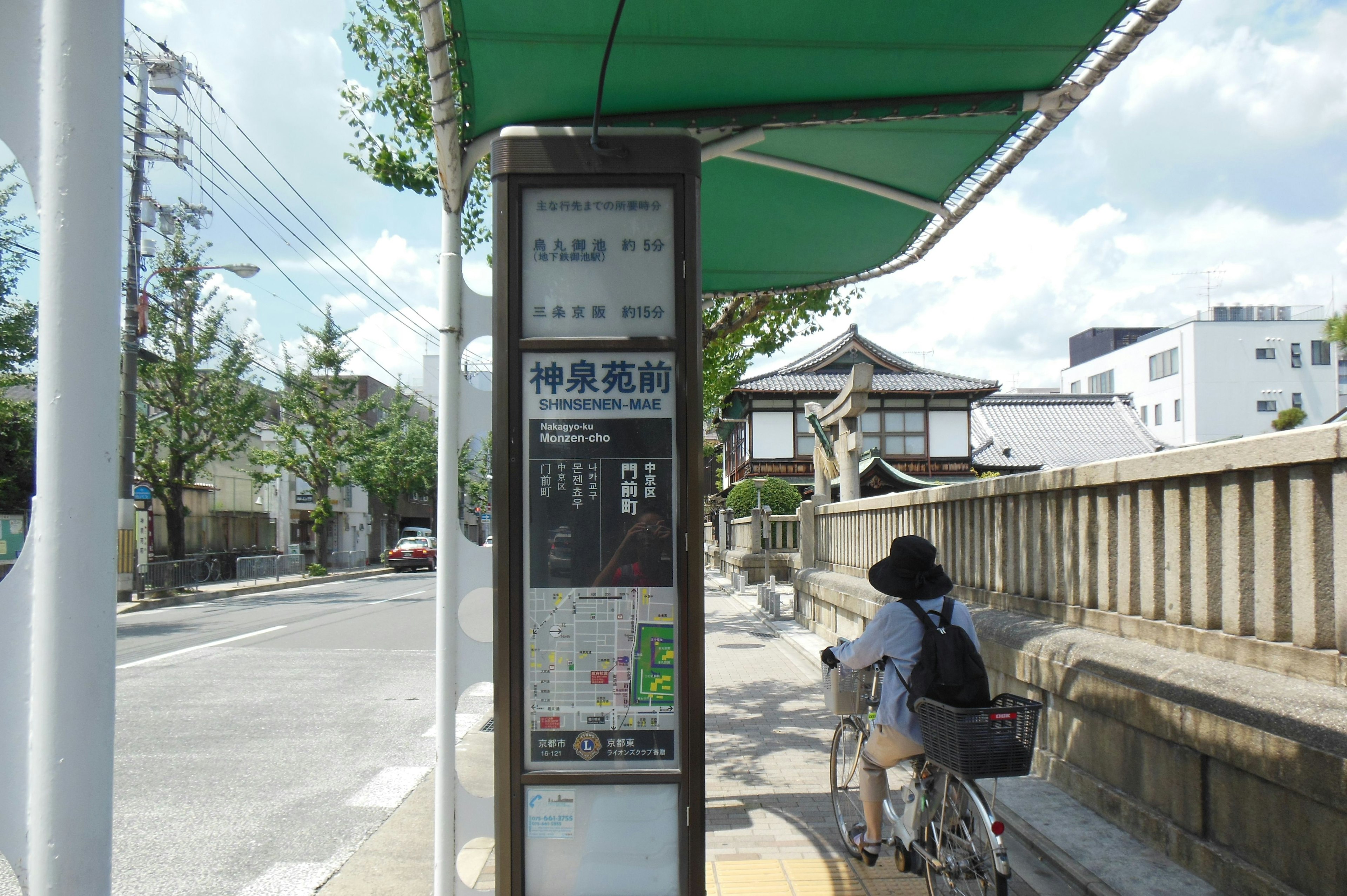 自転車に乗った人物がバス停の前にいる風景 バス停には時刻表と情報が掲示されている