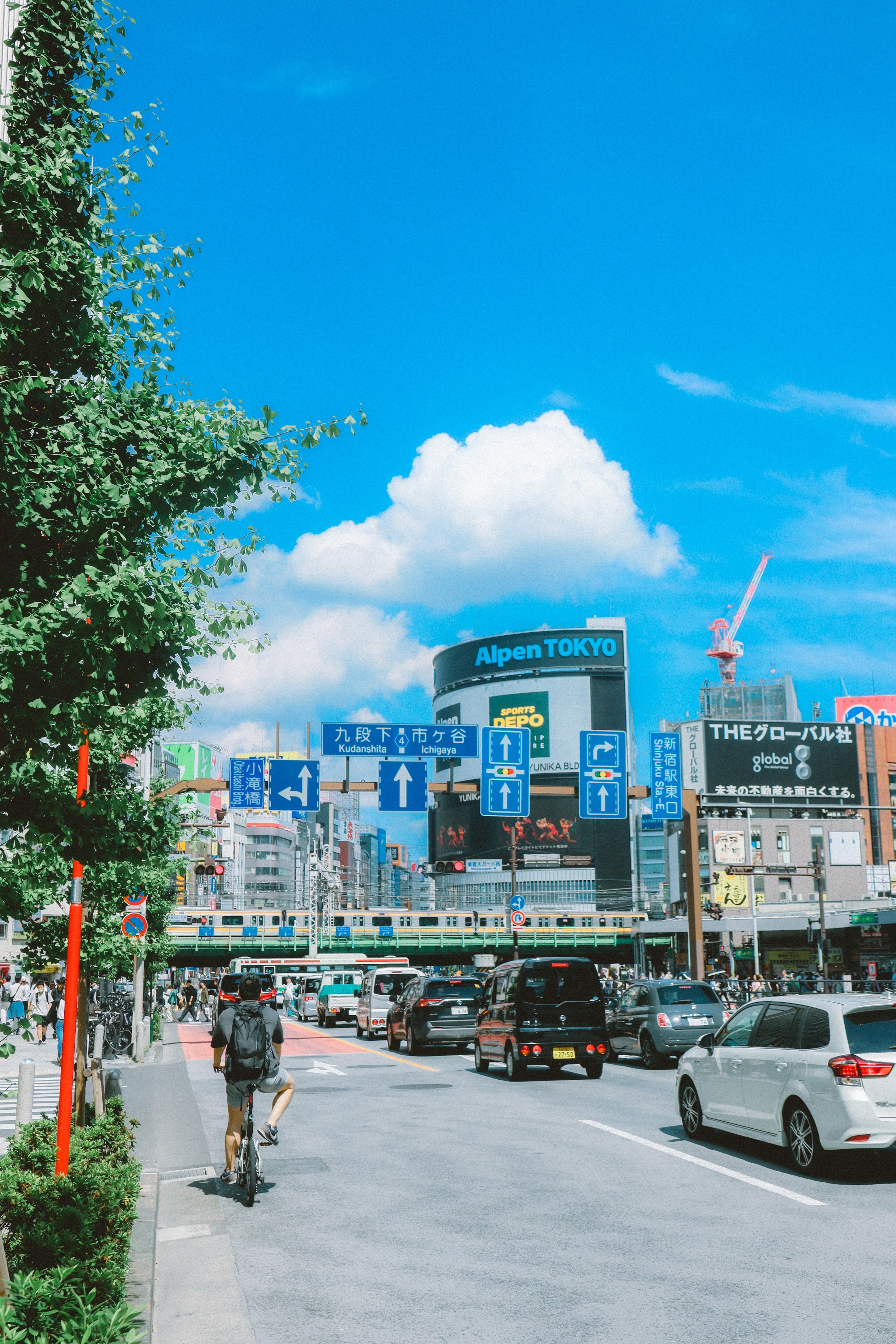 Pemandangan kota dengan langit biru dan awan Mobil dan tanda di sepanjang jalan Seseorang yang mengendarai sepeda di depan