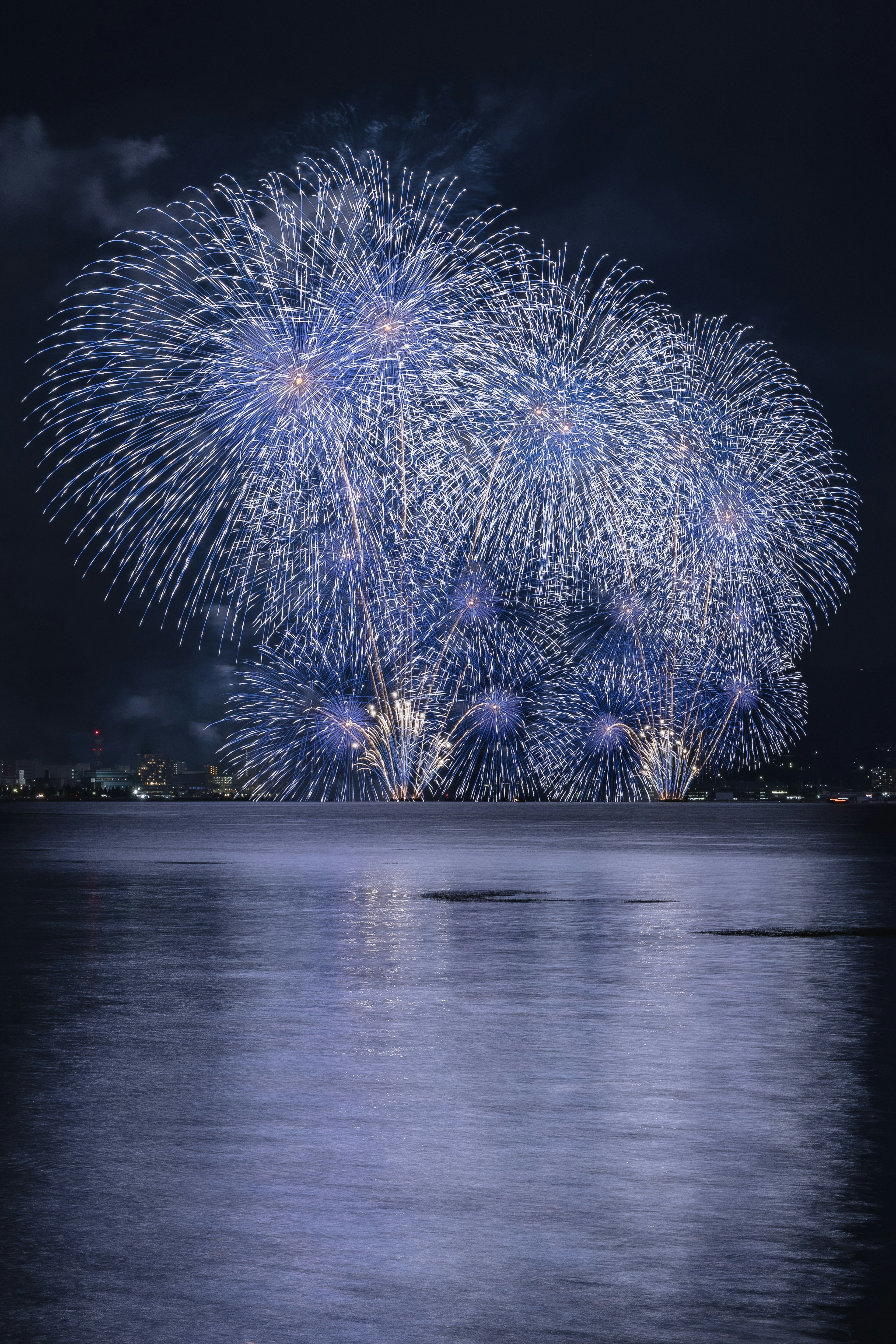 夜空に広がる青色の花火が水面に映る美しい風景