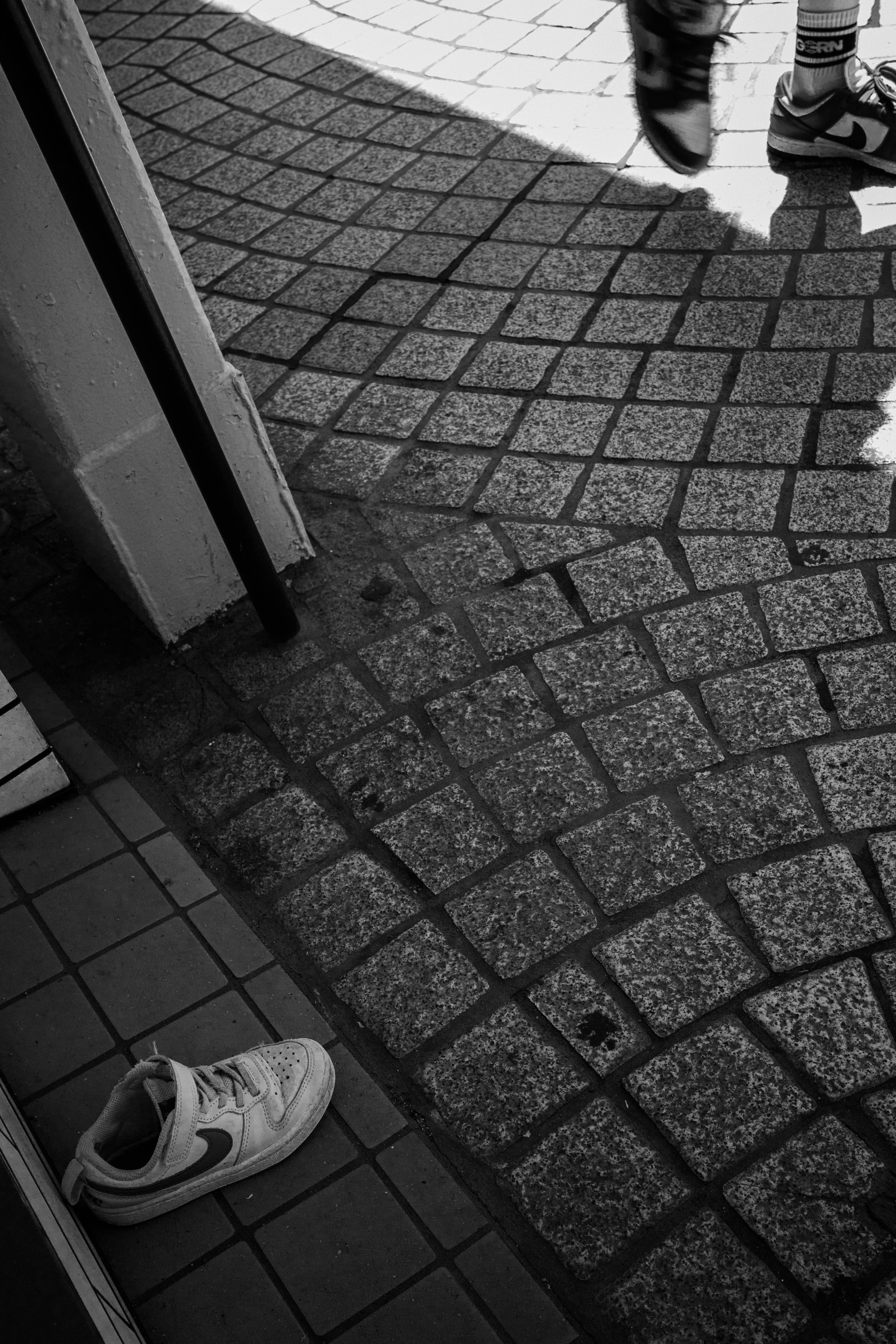 Baskets blanches posées à côté d'un chemin en pavés dans une photo en noir et blanc