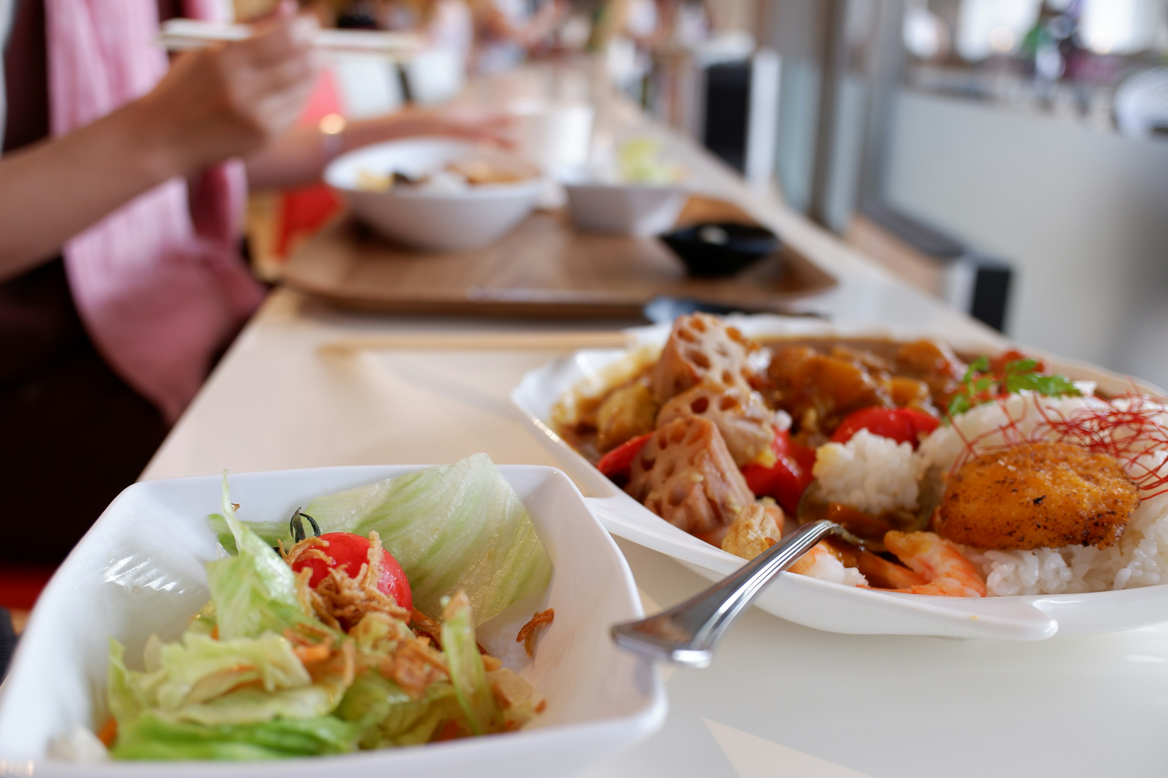 A salad and main dish on a table with a person eating