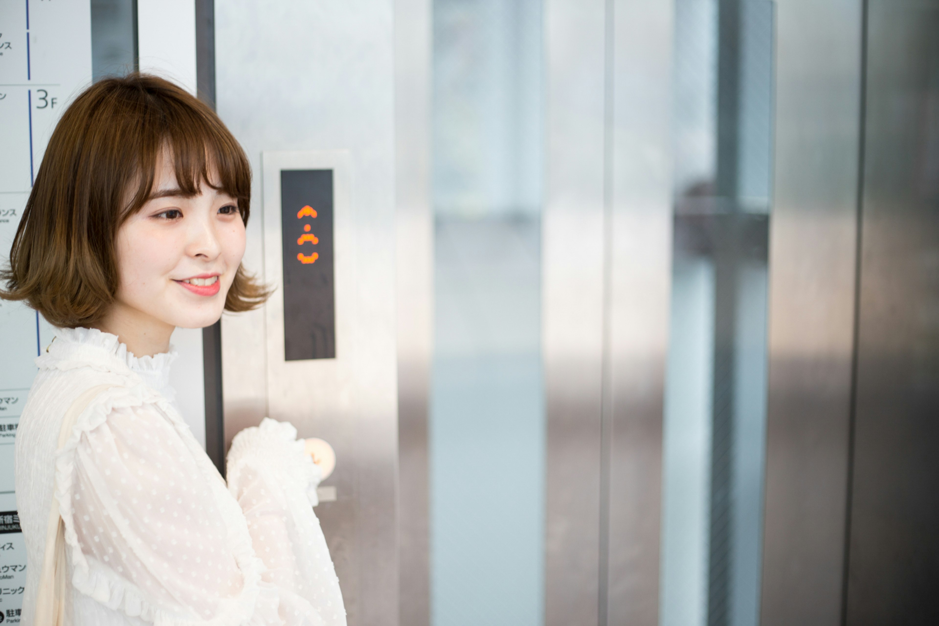 Mujer sonriendo frente a un ascensor con blusa blanca