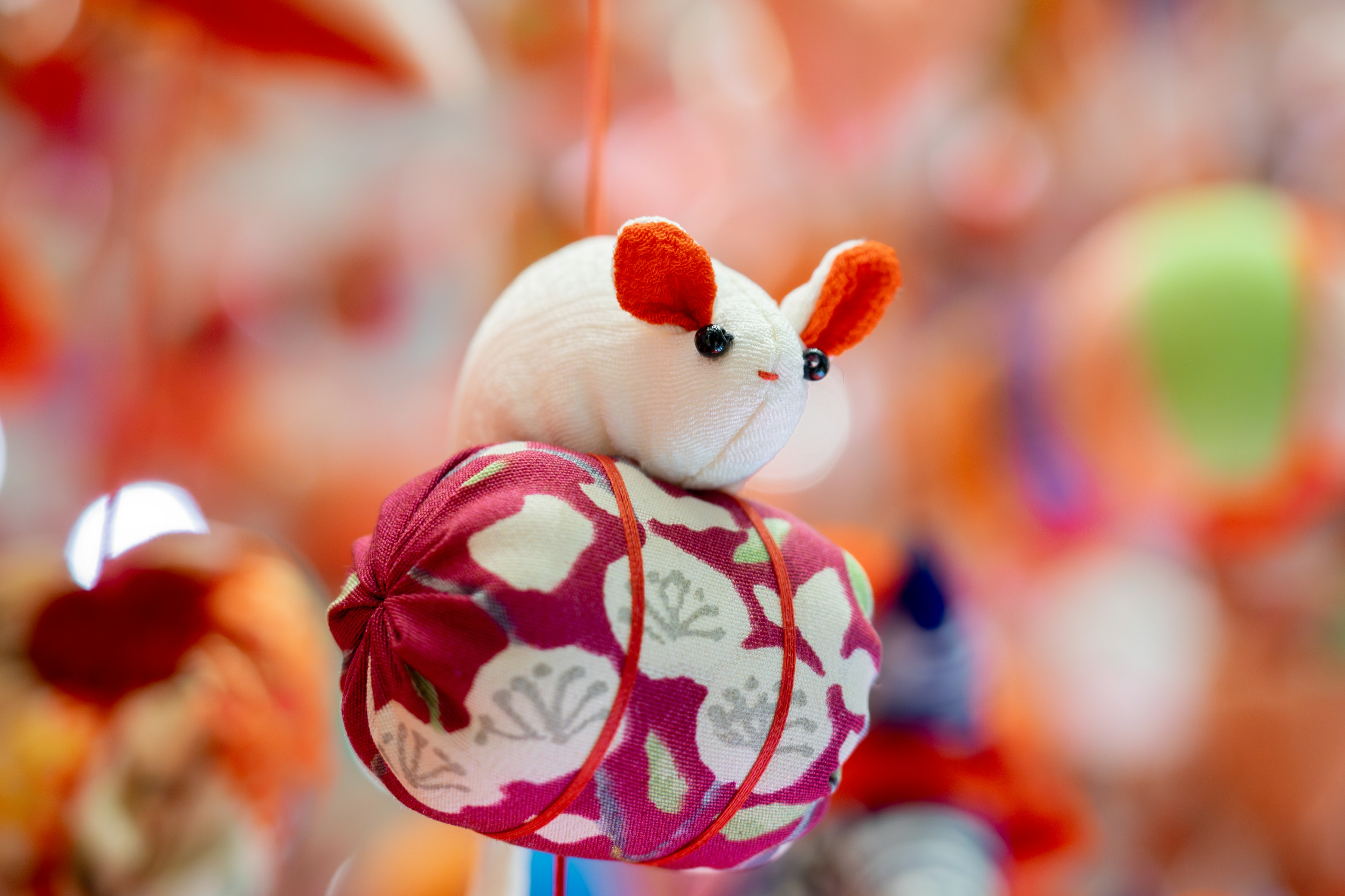 A plush mouse with red ears hanging against a colorful background