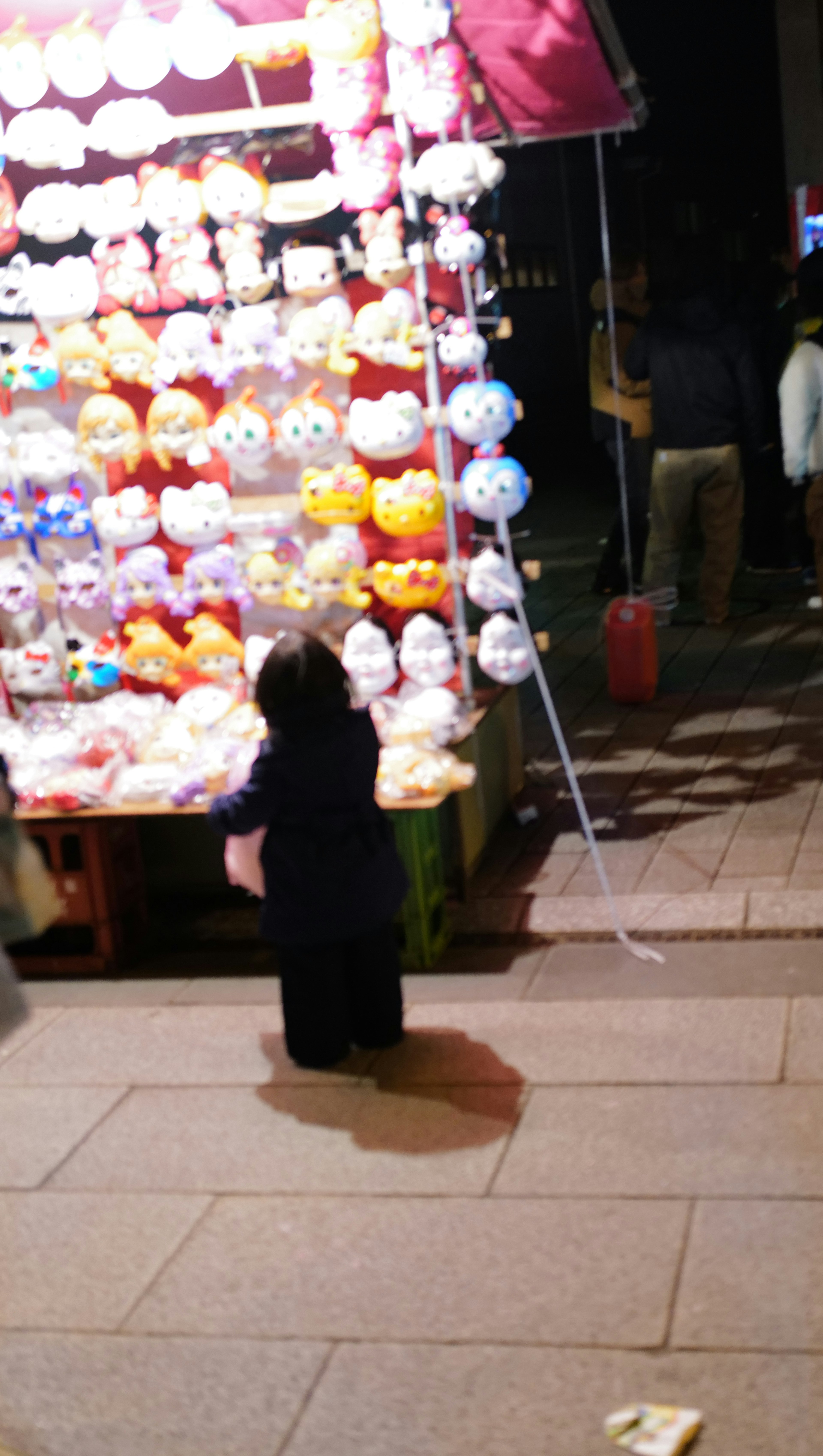 夜市でカラフルなぬいぐるみが並ぶ屋台とそれを見つめる子供