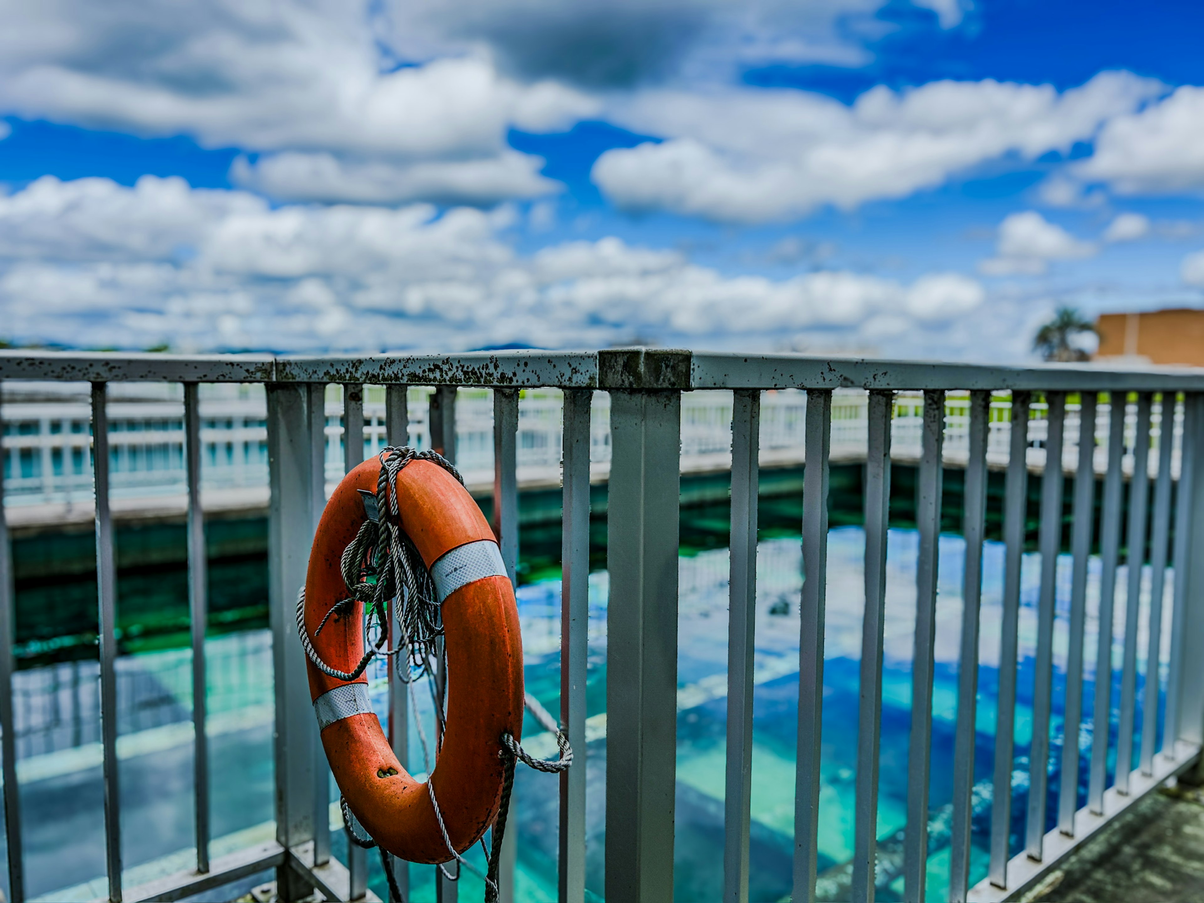 Lifebuoy hanging on a railing overlooking a clear water area under a blue sky