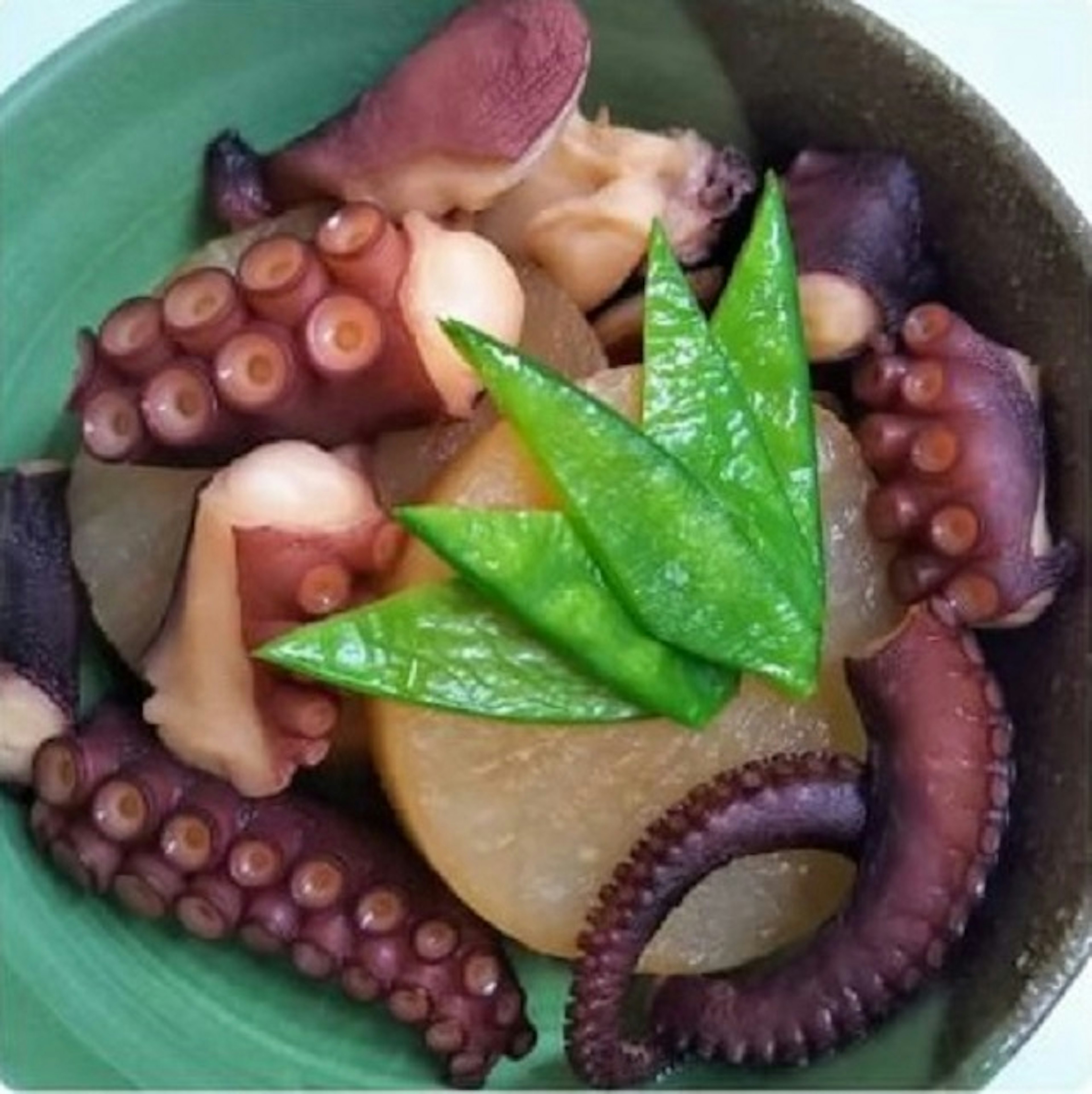 Un plat de poulpe servi dans une assiette verte avec des tentacules de poulpe et du radis blanc garni de pois sucrés