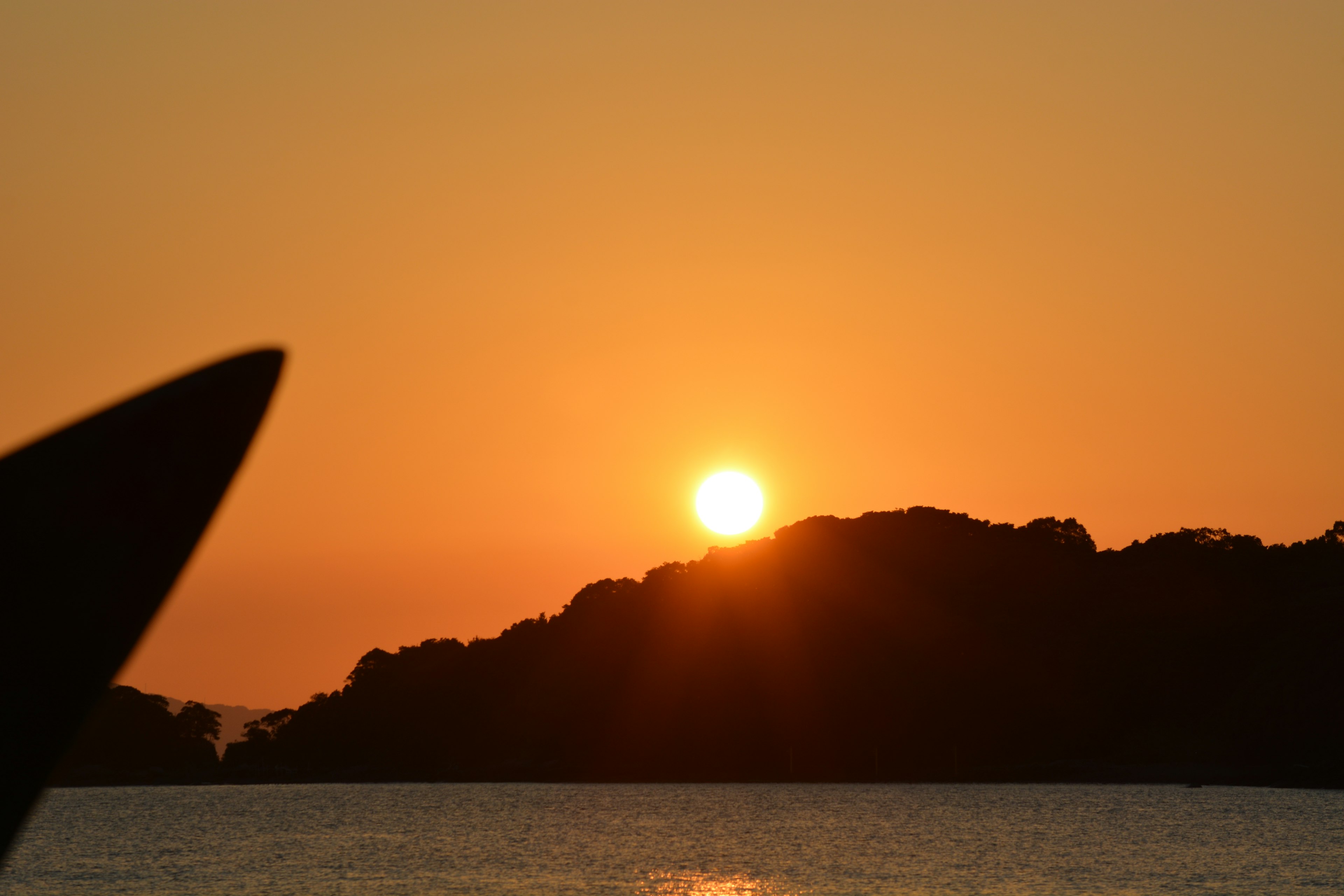 海に沈むオレンジ色の夕日とシルエットの山