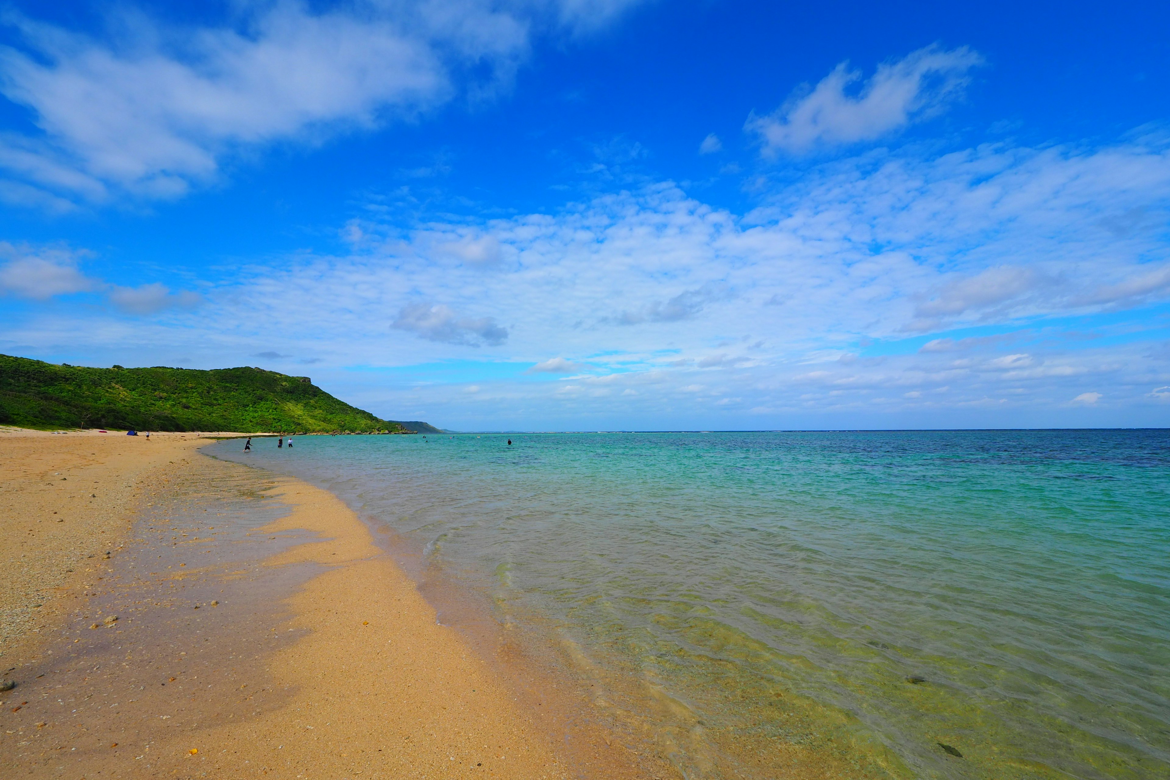 Scenic beach view with blue sky and clear ocean green hill in the background