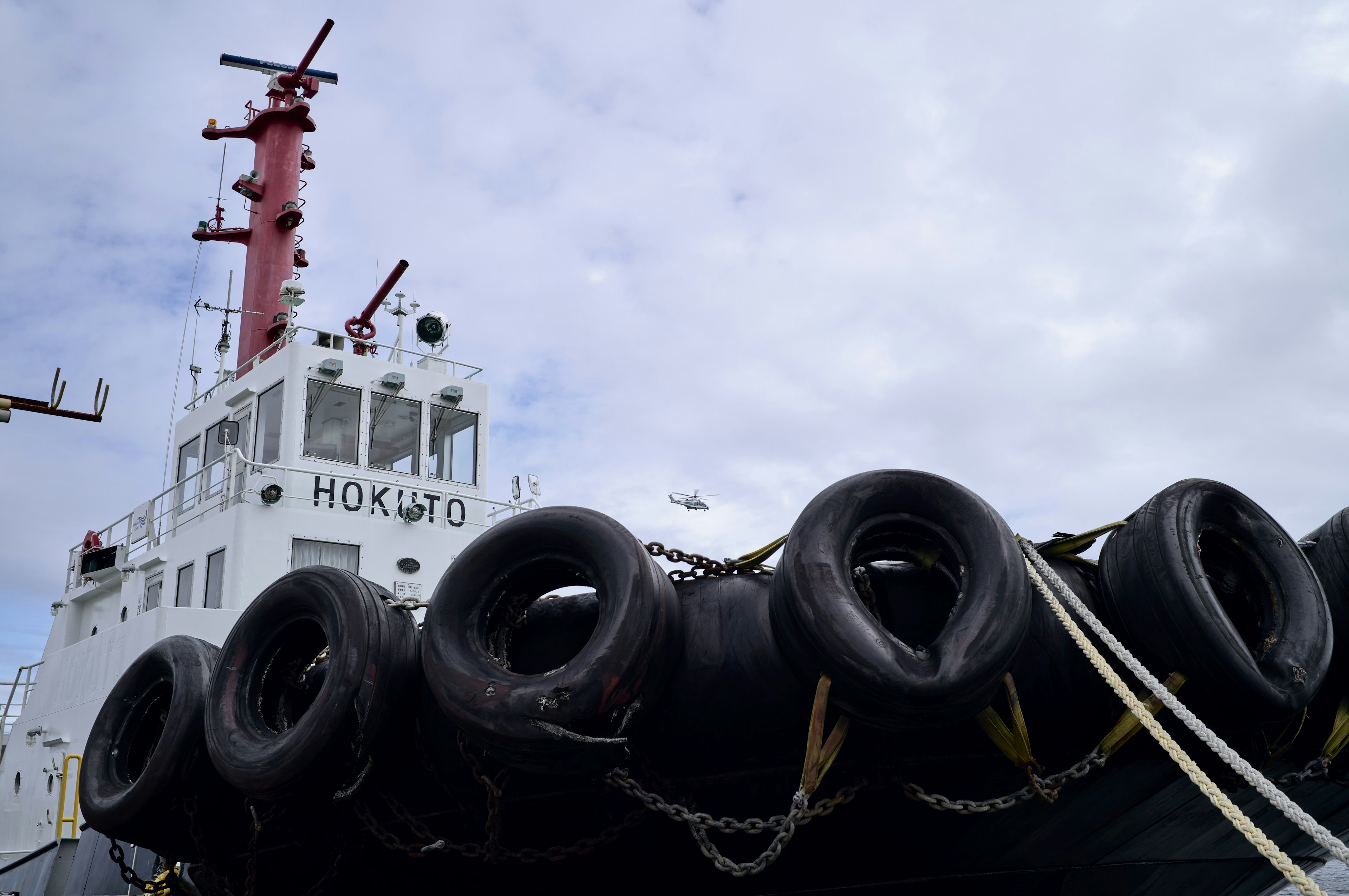 Tugboat HOKUTO with black tires and red mast against cloudy sky