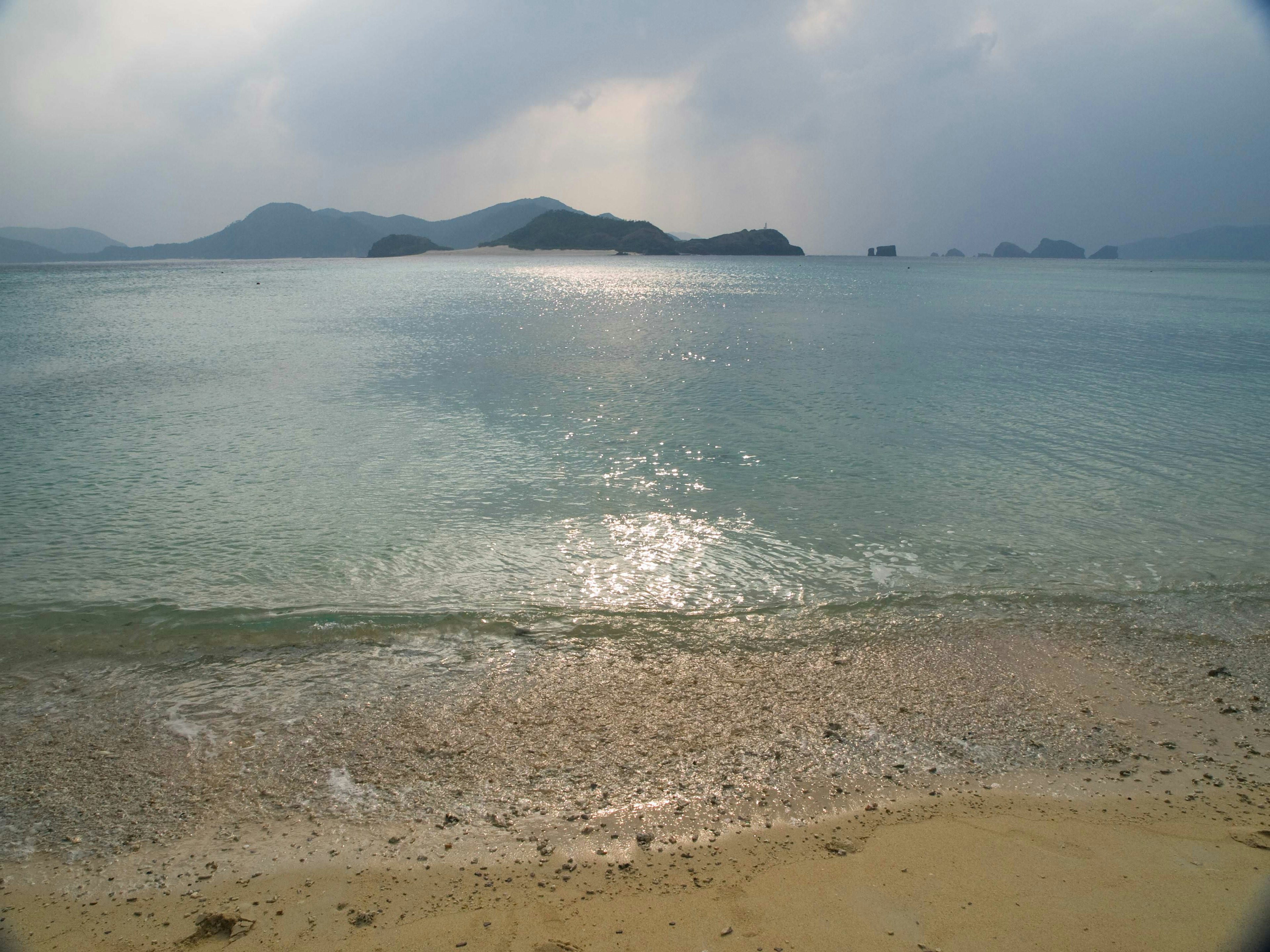 ทิวทัศน์ชายหาดที่เงียบสงบพร้อมคลื่นที่อ่อนโยนและเกาะที่อยู่ไกลออกไป