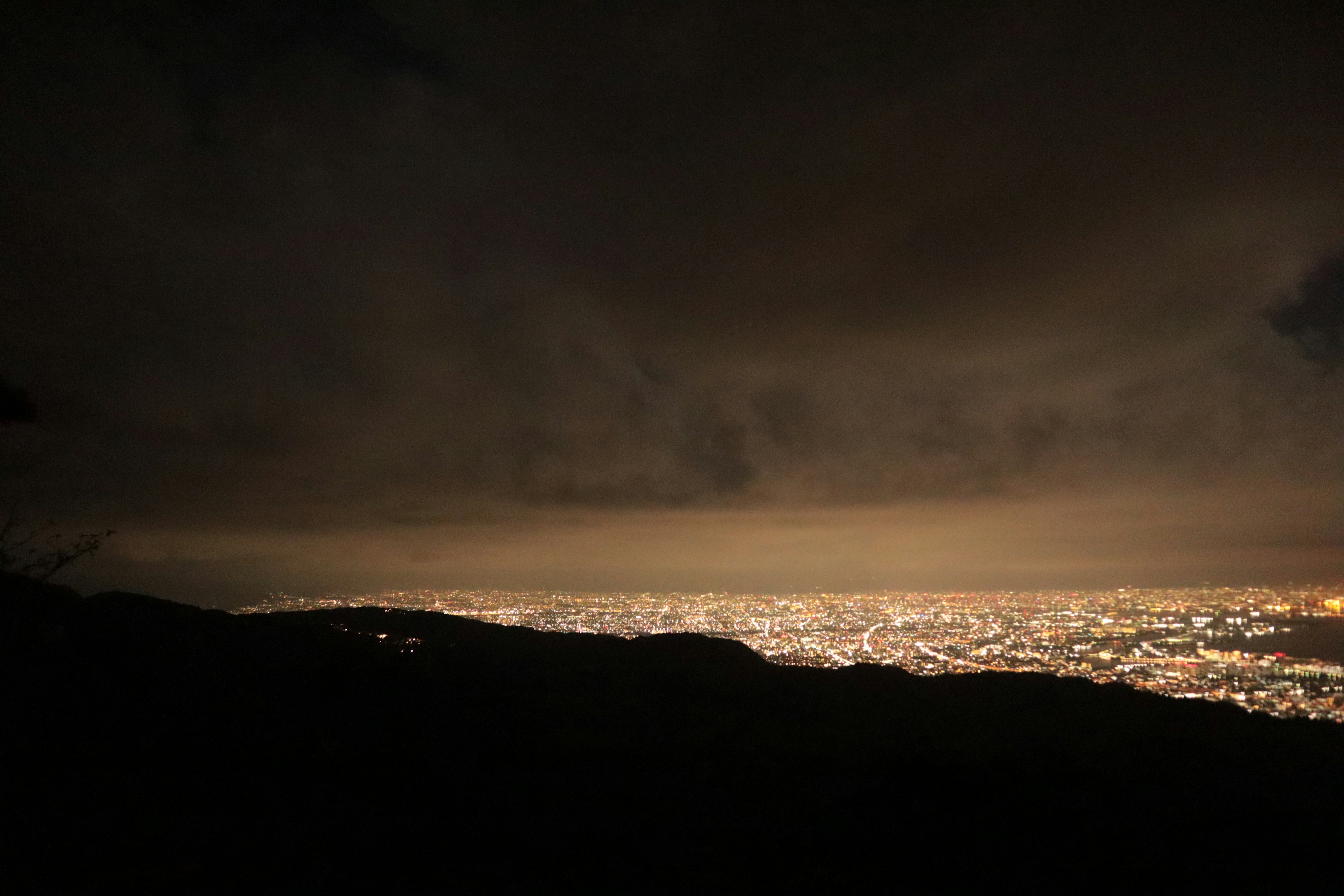 Vista notturna delle luci della città che si estendono all'orizzonte cielo scuro e silhouette di montagna