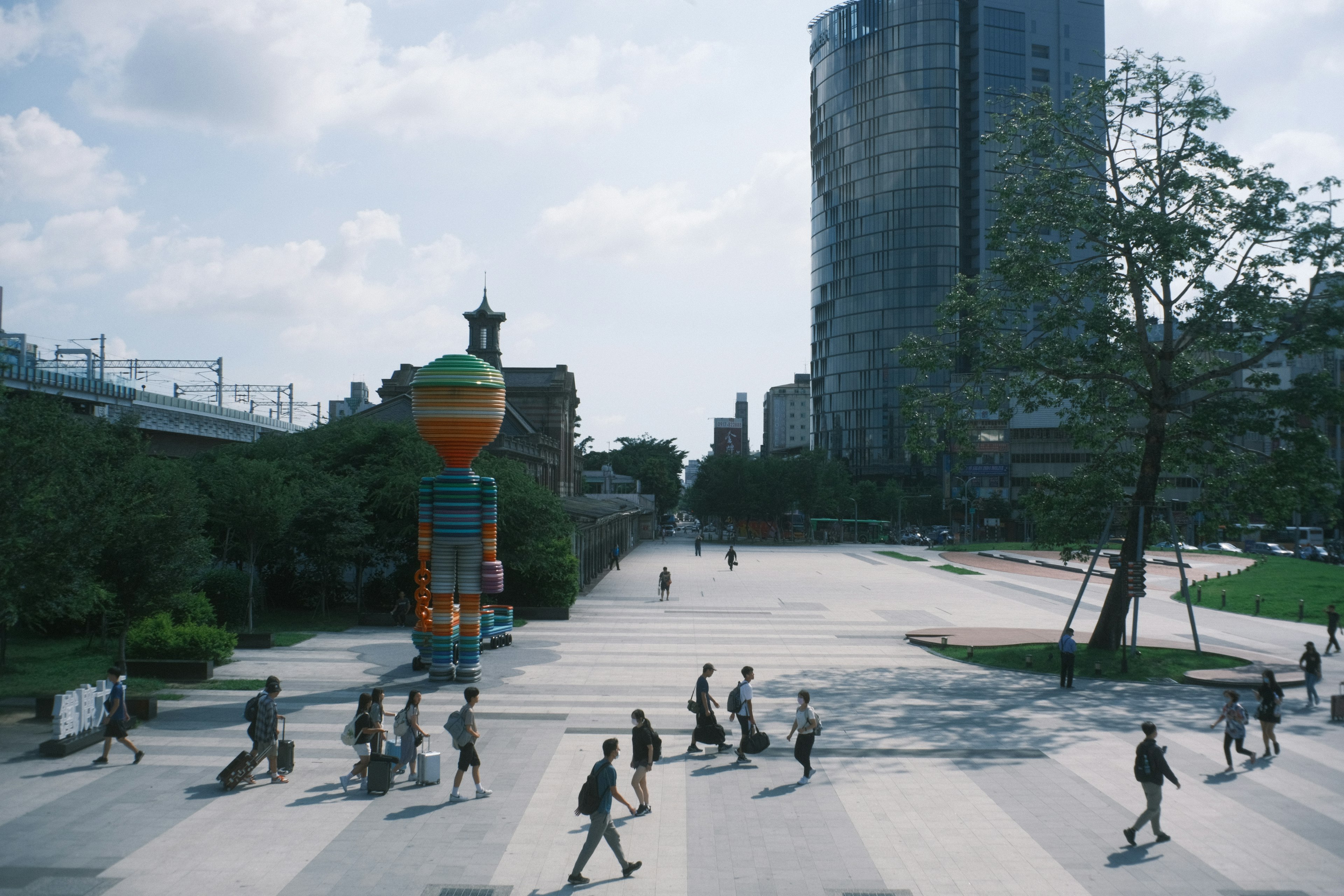 Una scena di persone che camminano in una piazza del parco con un oggetto colorato e grattacieli sullo sfondo