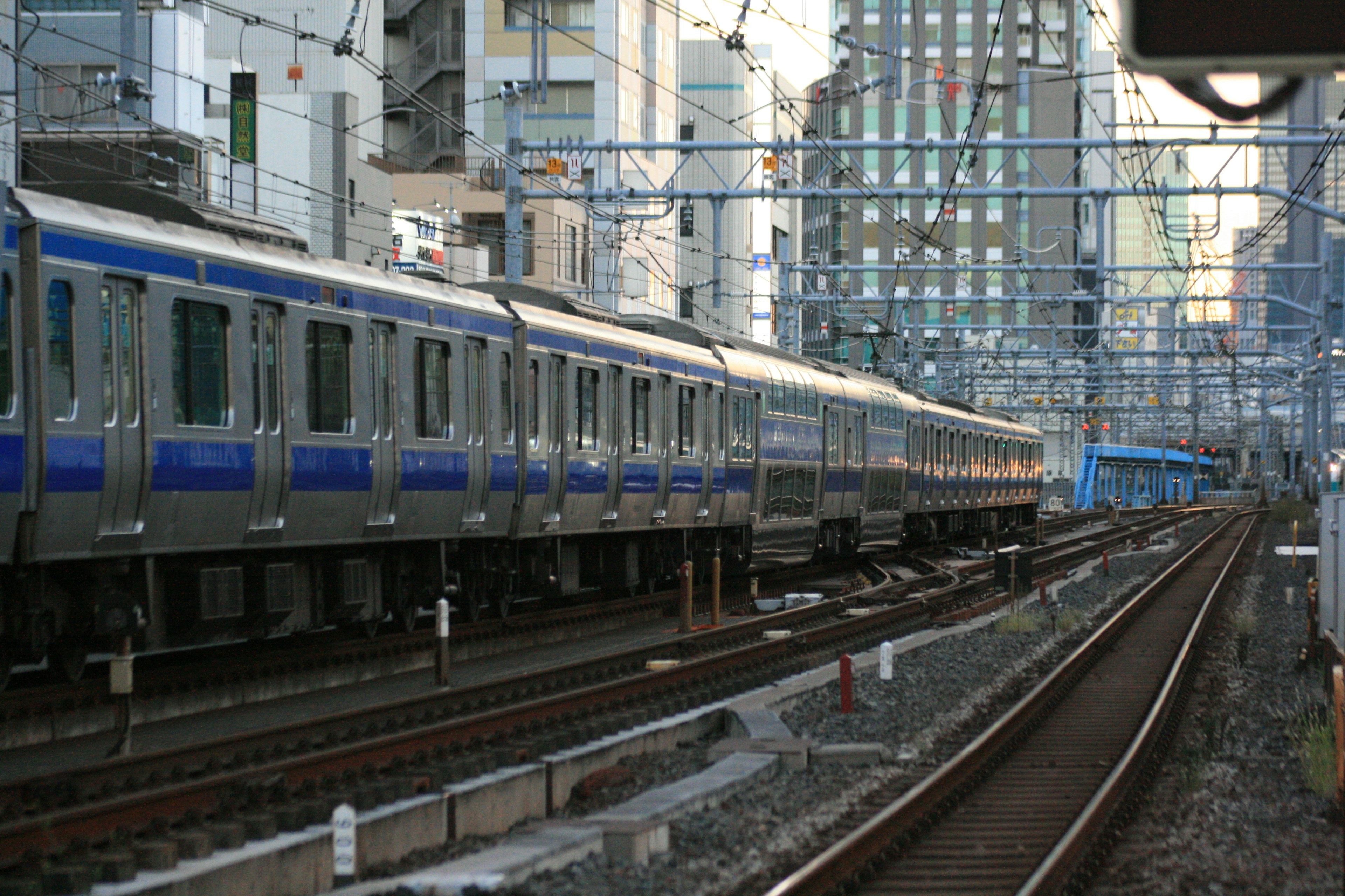 Silver train with blue stripes running alongside a city backdrop