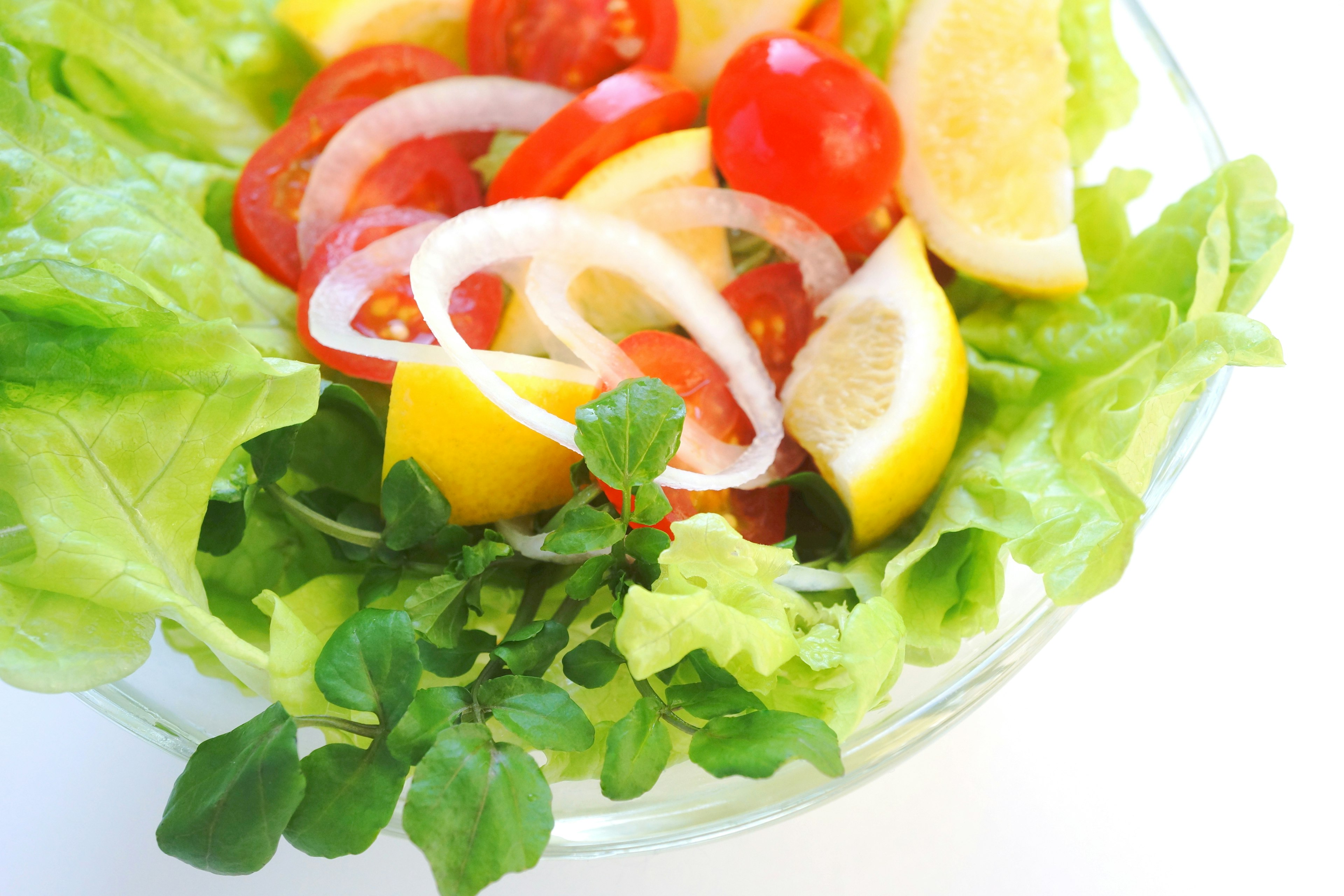 A bowl of fresh salad featuring lettuce, tomatoes, lemon, onion, and oregano