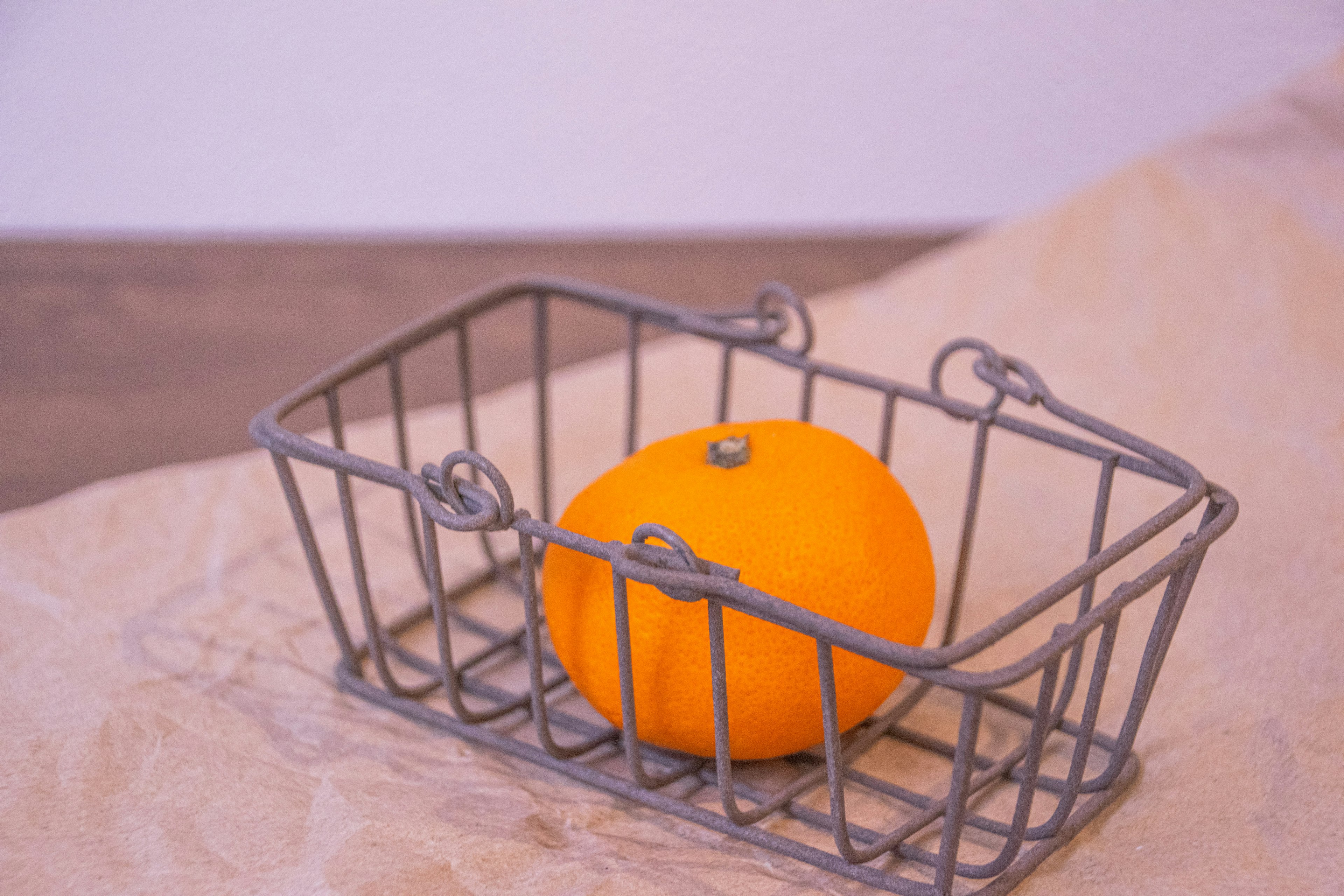 Une orange placée dans un panier en métal sur une table