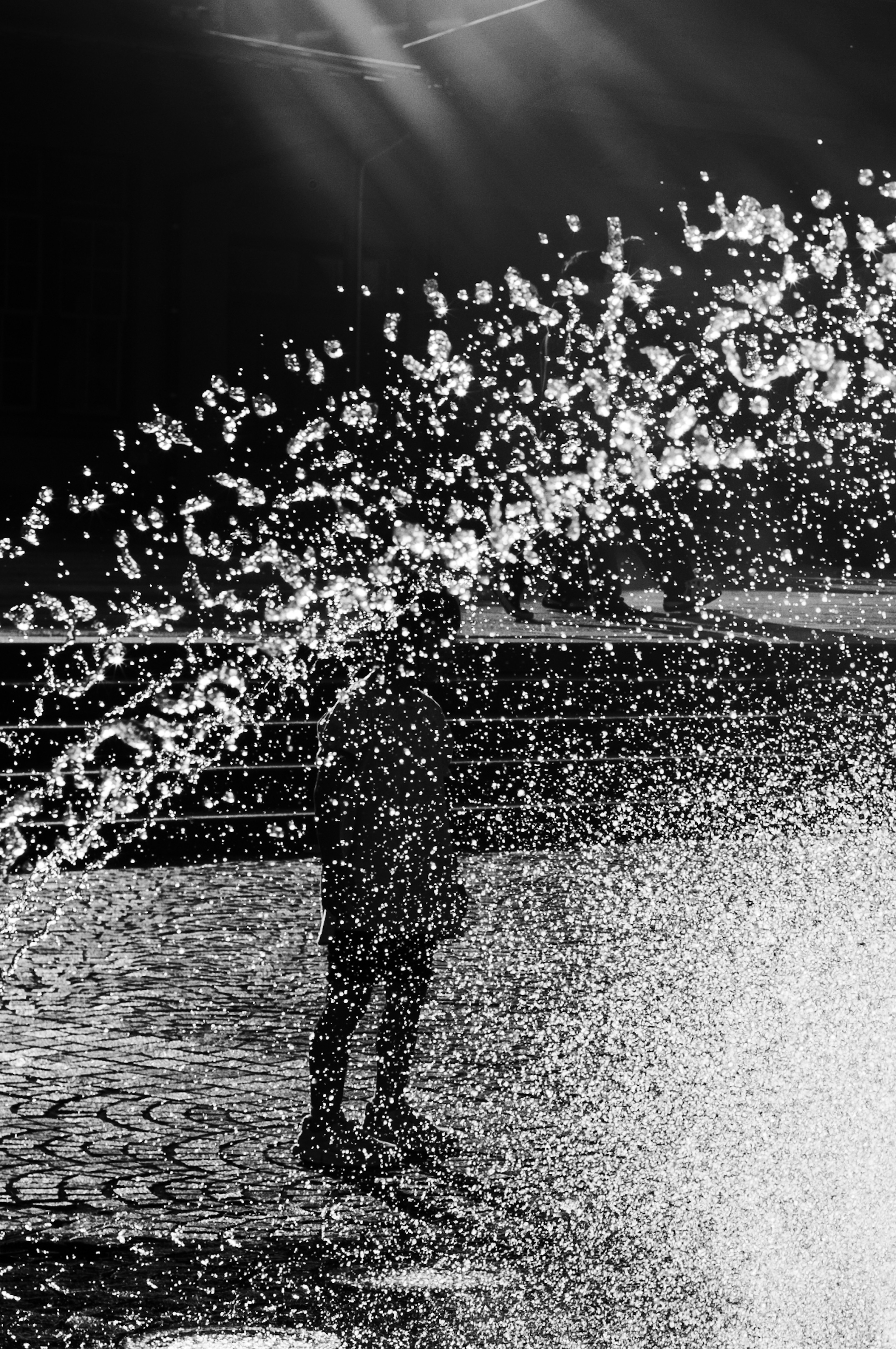 Foto in bianco e nero di una figura che si muove tra schizzi d'acqua e luce