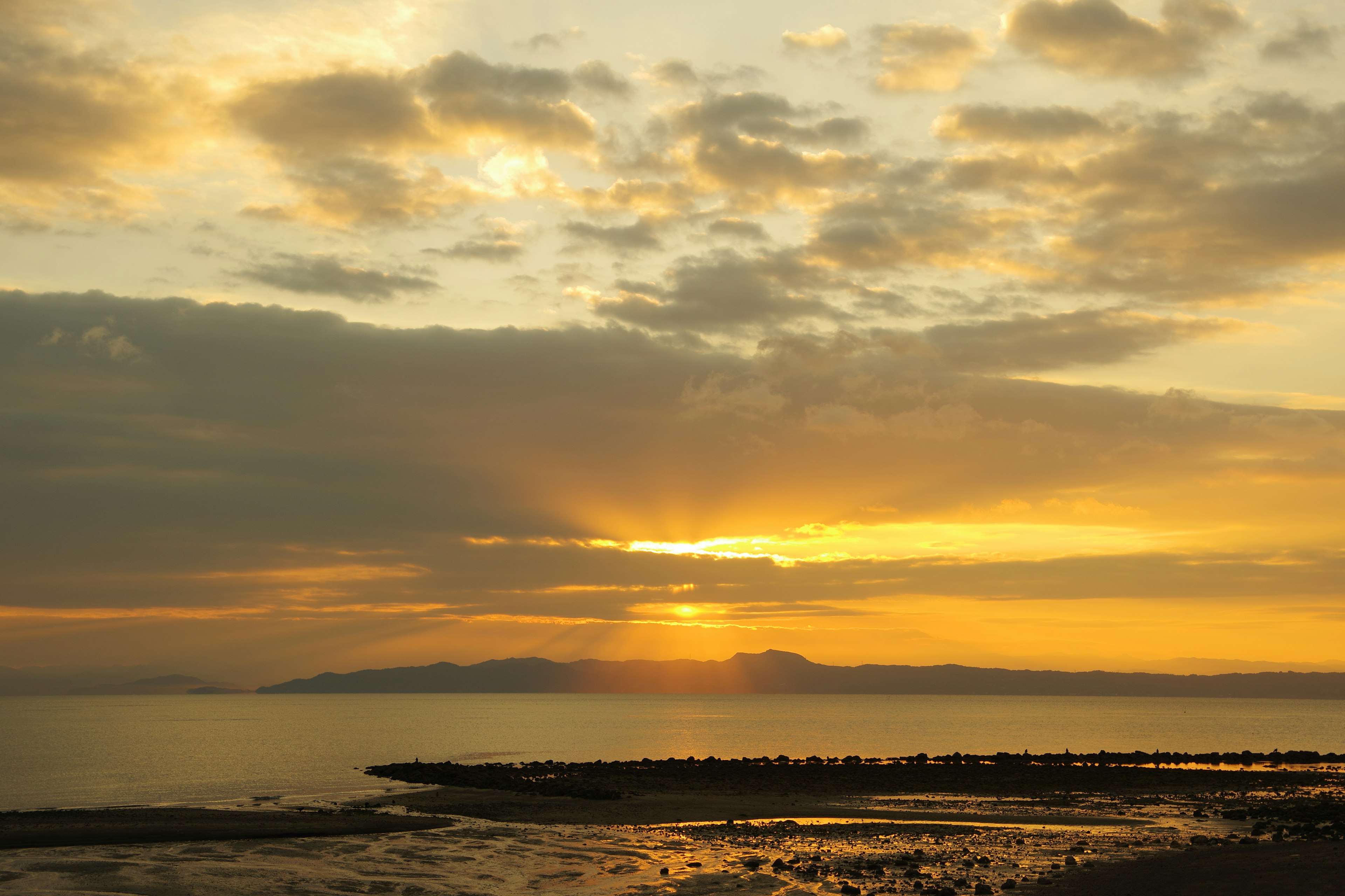 Schöner Sonnenuntergang über dem Meer mit Lichtstrahlen, die durch die Wolken scheinen, und ruhiger Wasseroberfläche