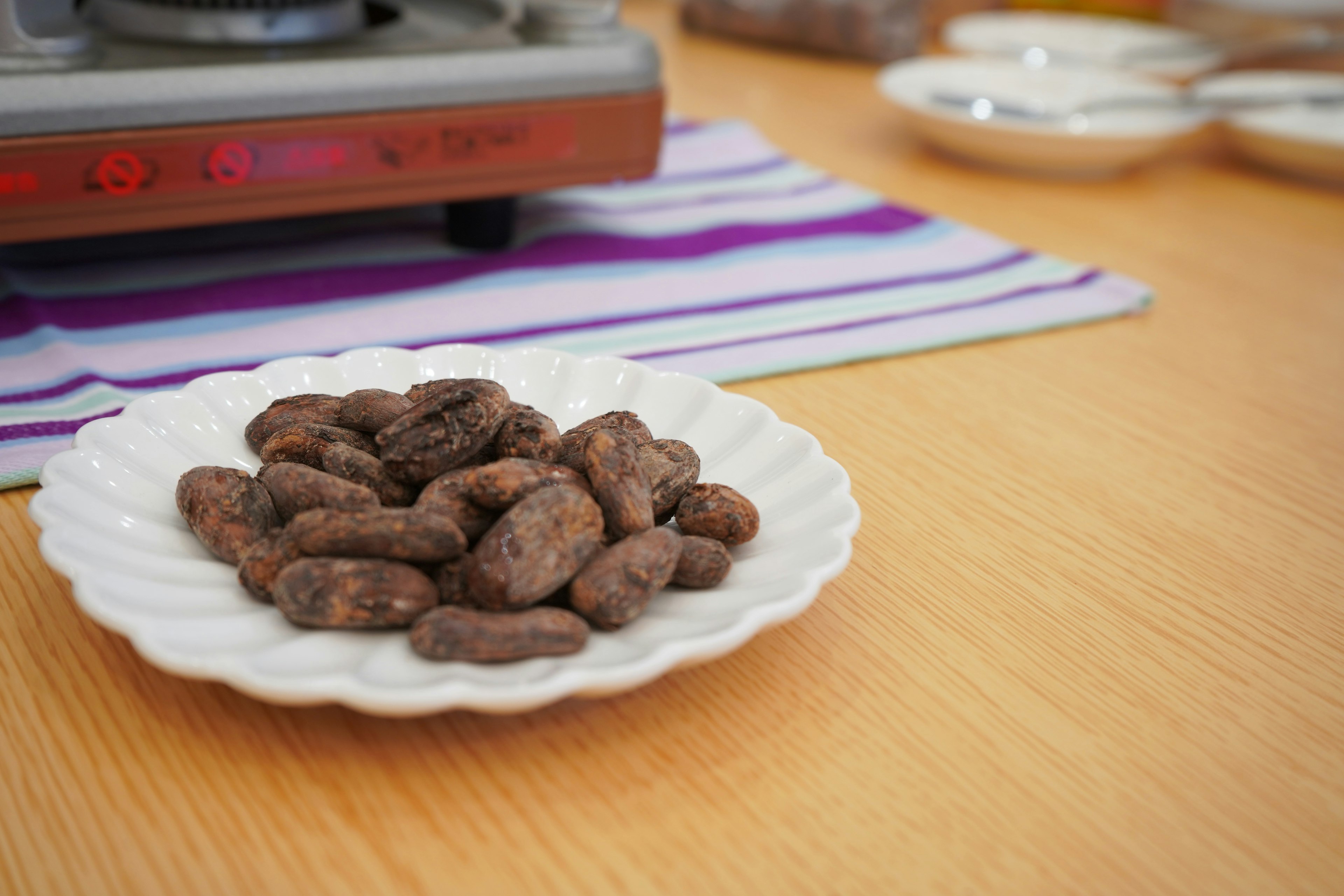 A plate of cocoa beans placed on a wooden table with a cooking stove in the background