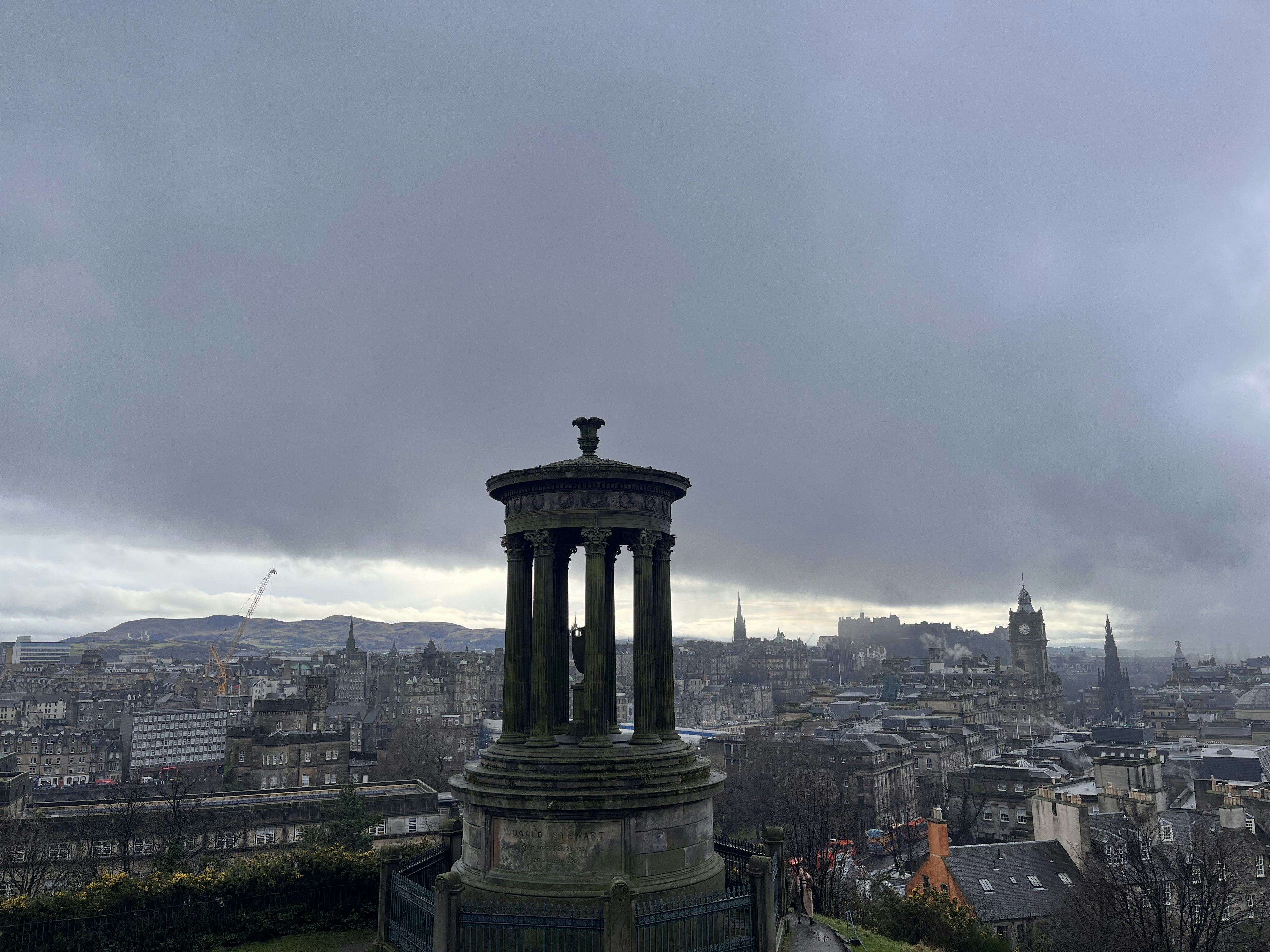 Pemandangan kota Edinburgh dengan langit mendung dan monumen di latar depan