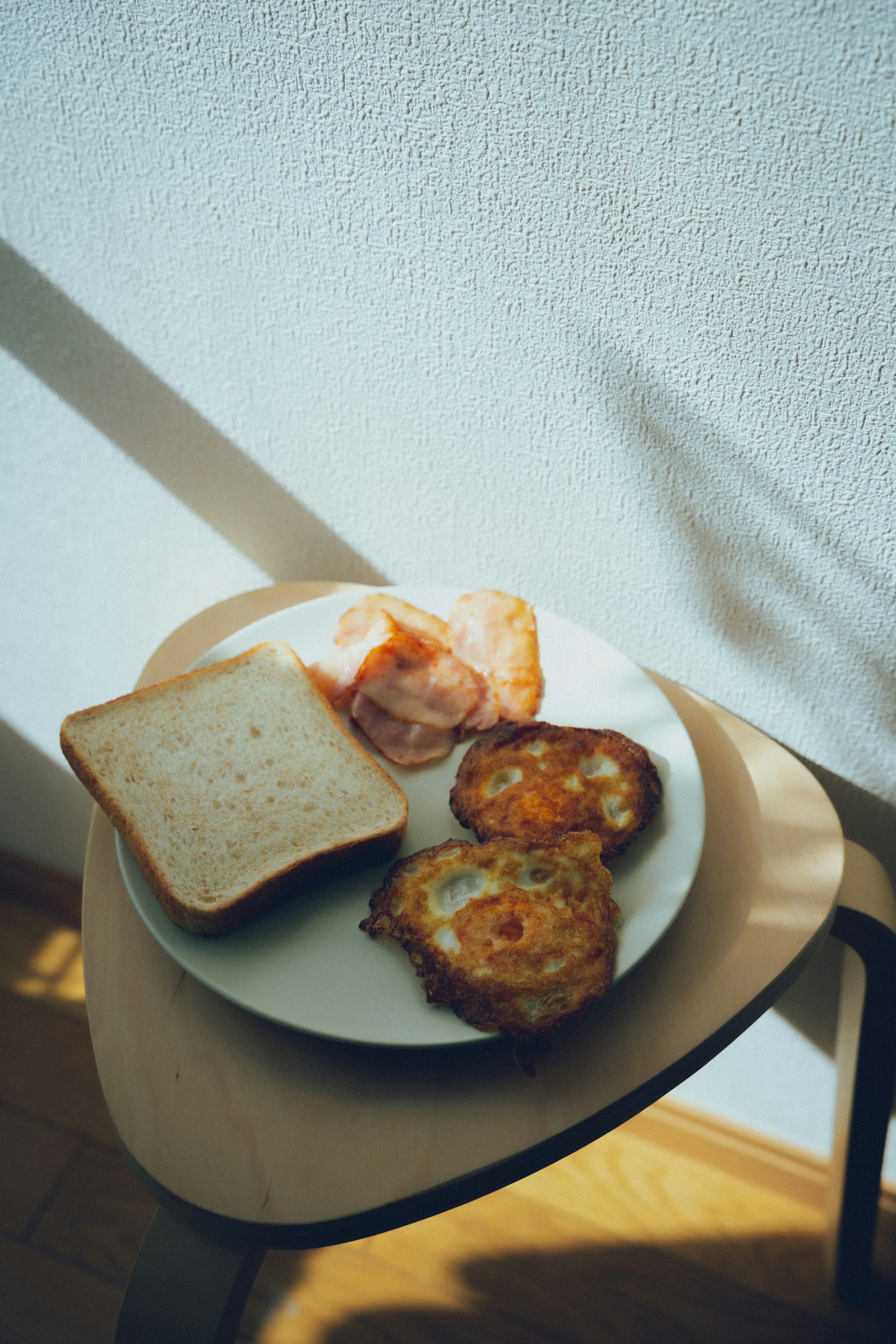 Plate with toast and fried eggs on a small table against a white wall