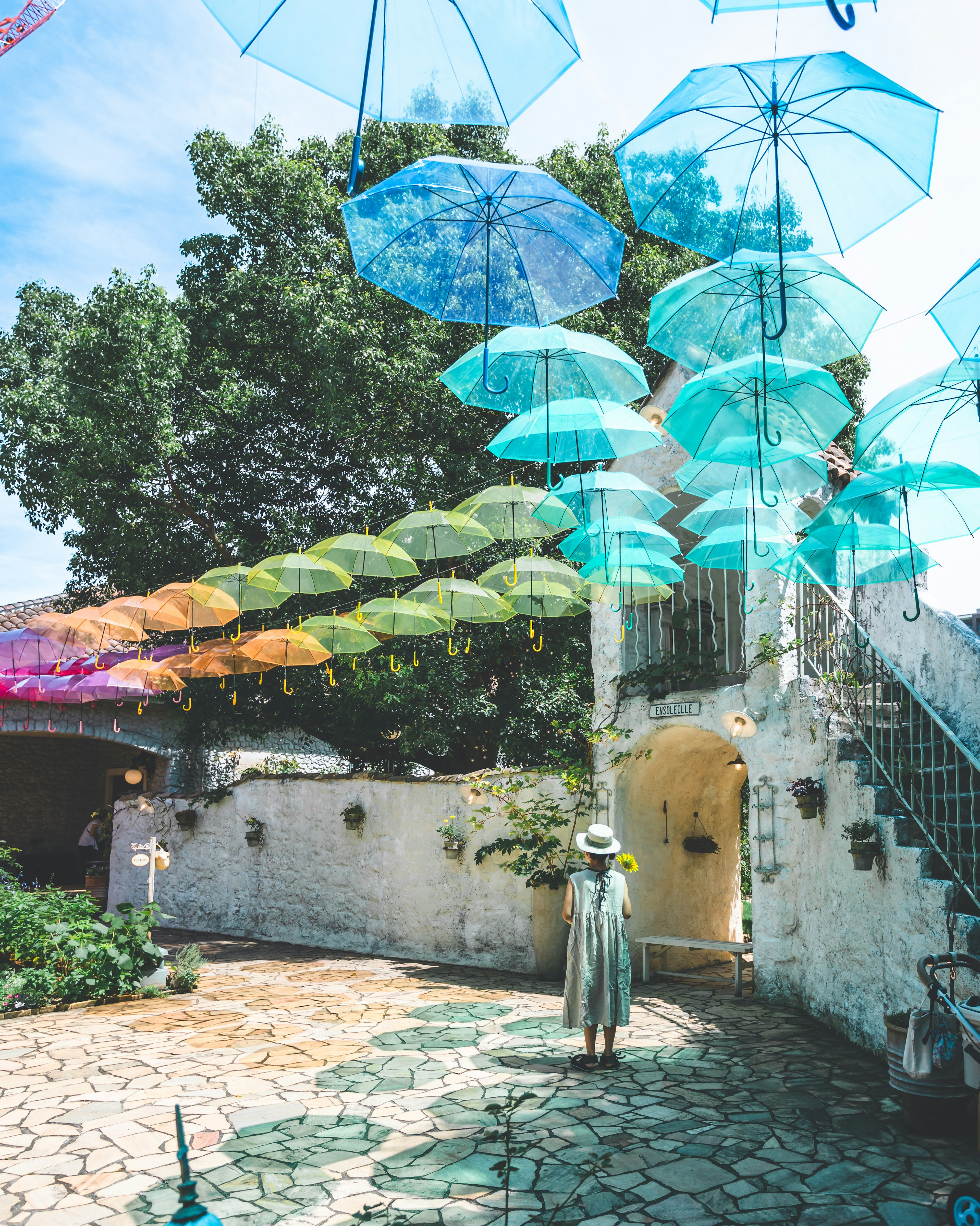 A woman standing in a garden with colorful umbrellas hanging overhead