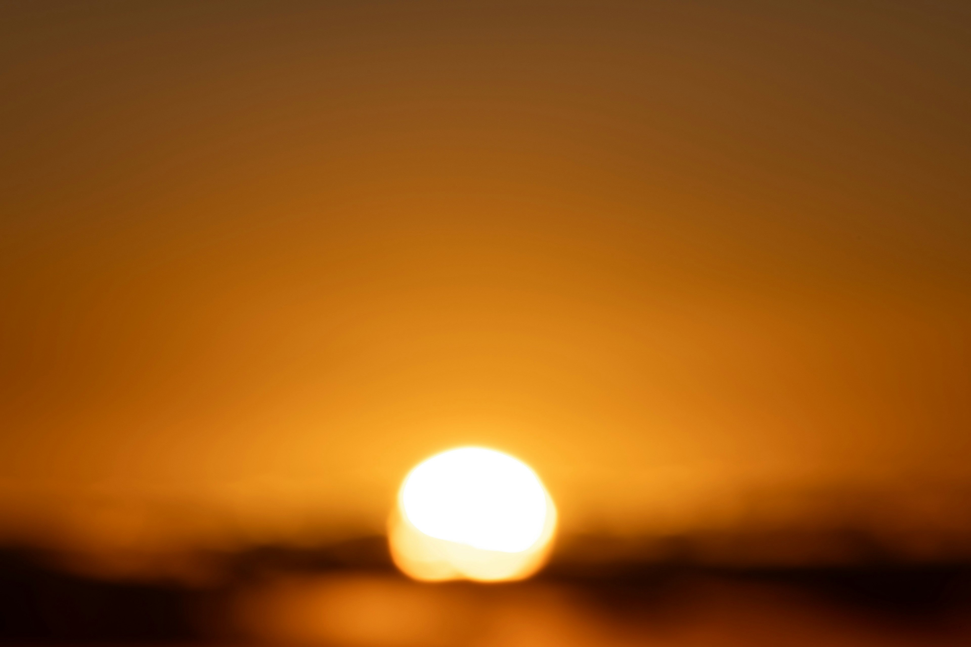 ぼやけた夕日がオレンジ色の空に沈む様子