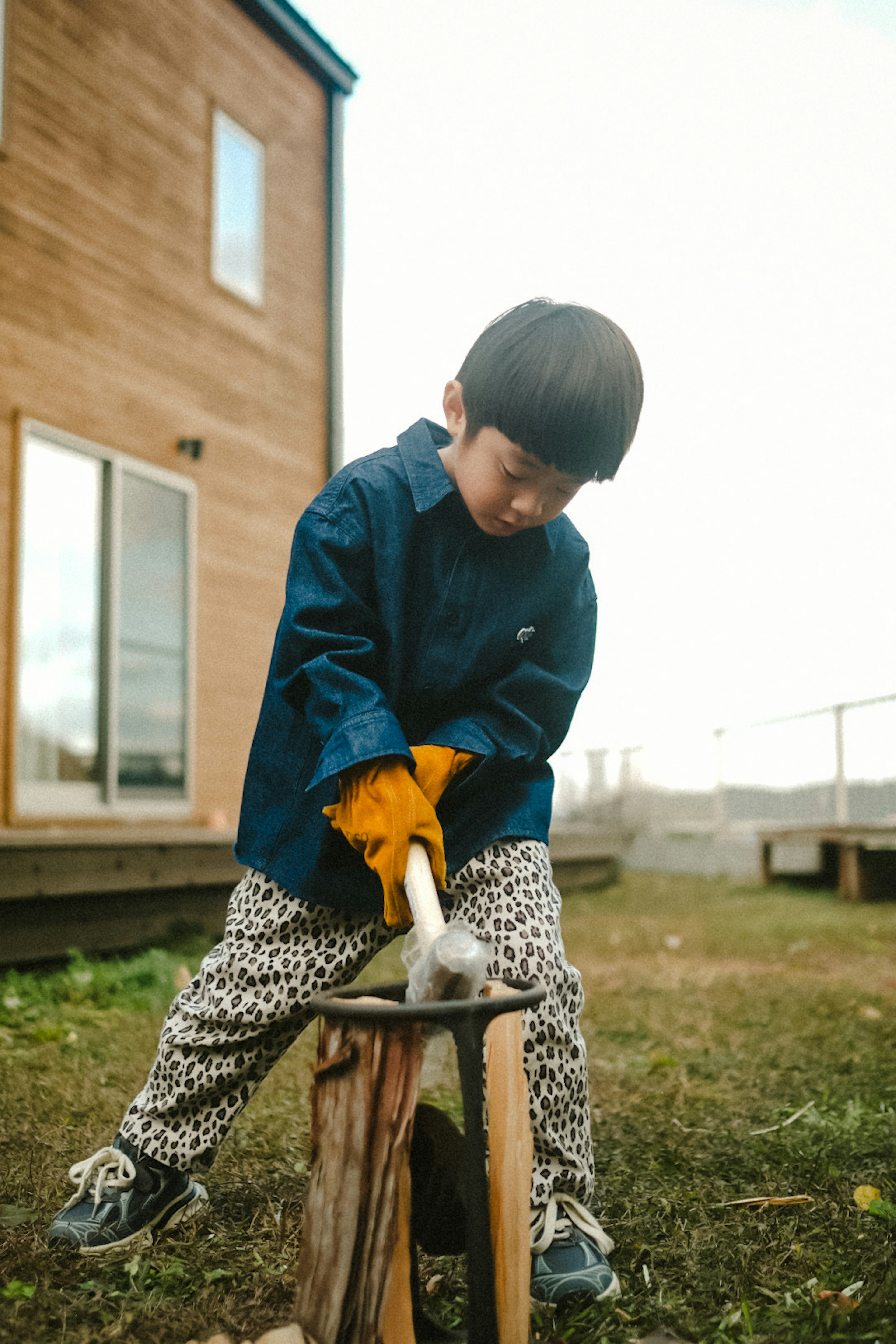 孩子在一根原木上使用锤子，穿着蓝色衬衫和黄色手套